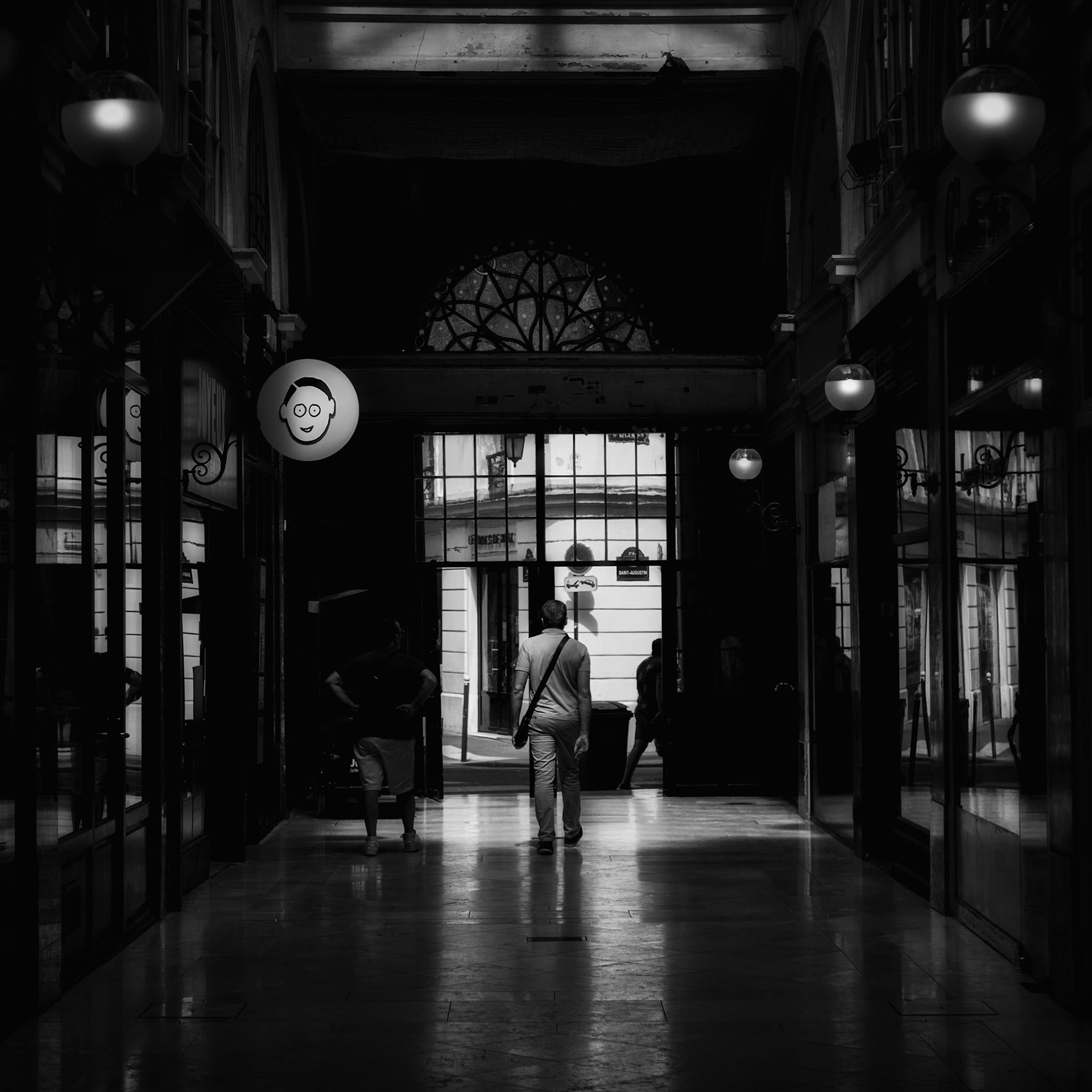 Observed Passage at Passage Choiseul, Paris. A pedestrian moving through the covered arcade beneath a face-like shop sign.