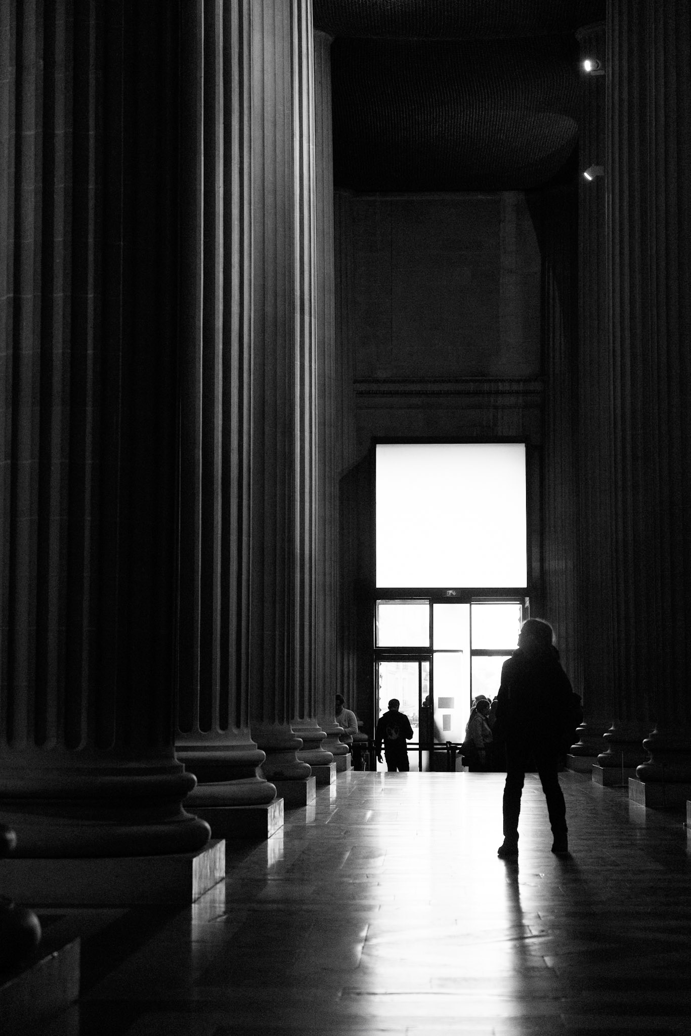 A figure walking between the monumental columns of the Panthéon, toward the light