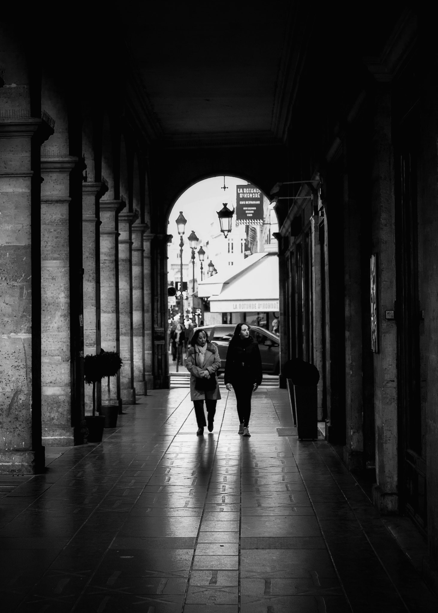 Rue de Rivoli, Paris. Two pedestrians walking beneath the arcades toward the brighter street beyond.