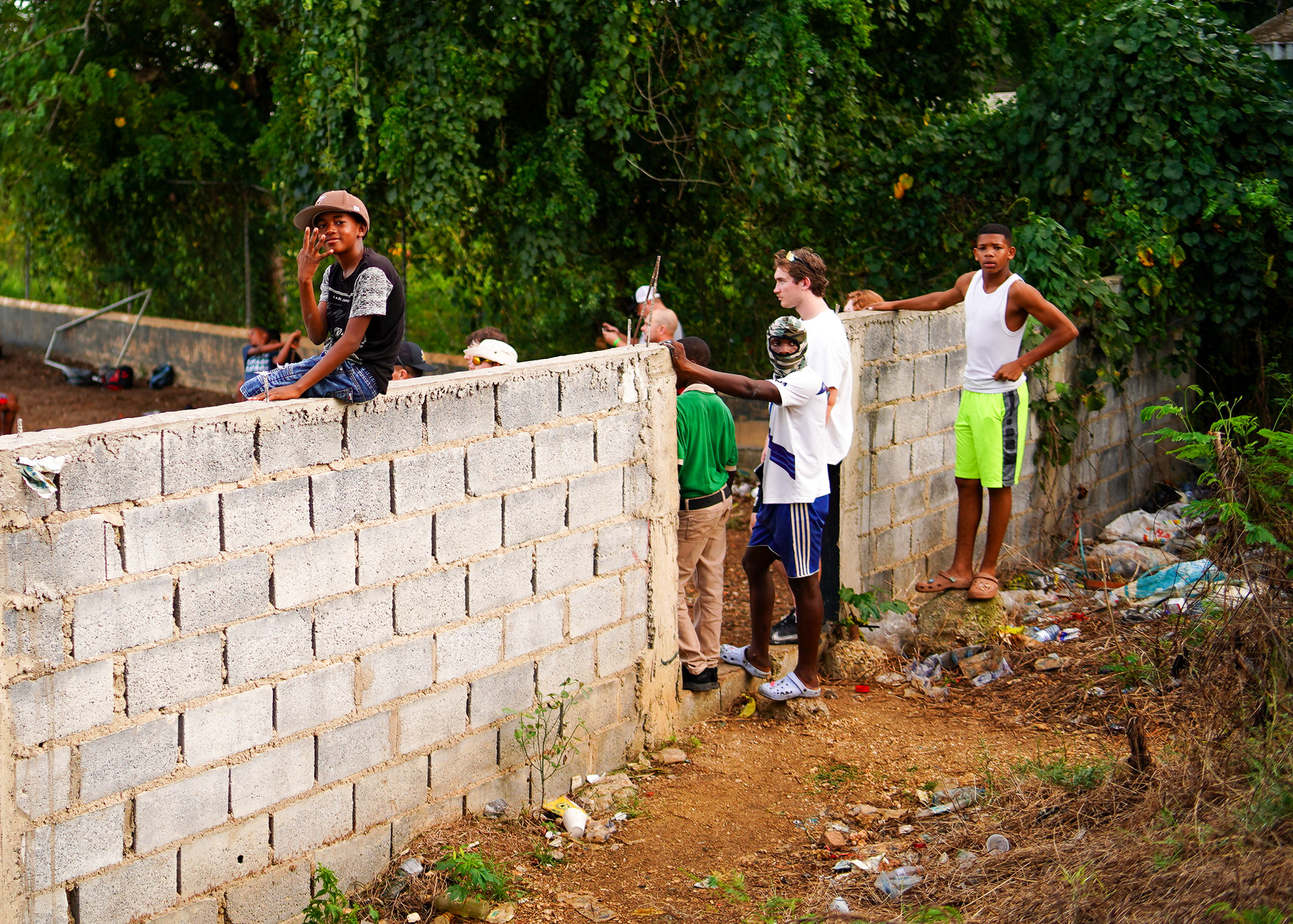 Locals watch batting practice from behind a brick wall.