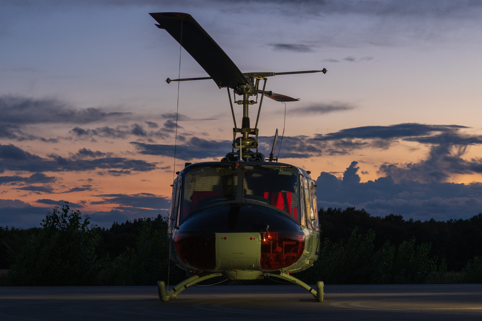 Bell UH-1 Iroquois frontaanzicht op de tarmac, met rood verlichte cockpit en een dramatische avondschemering