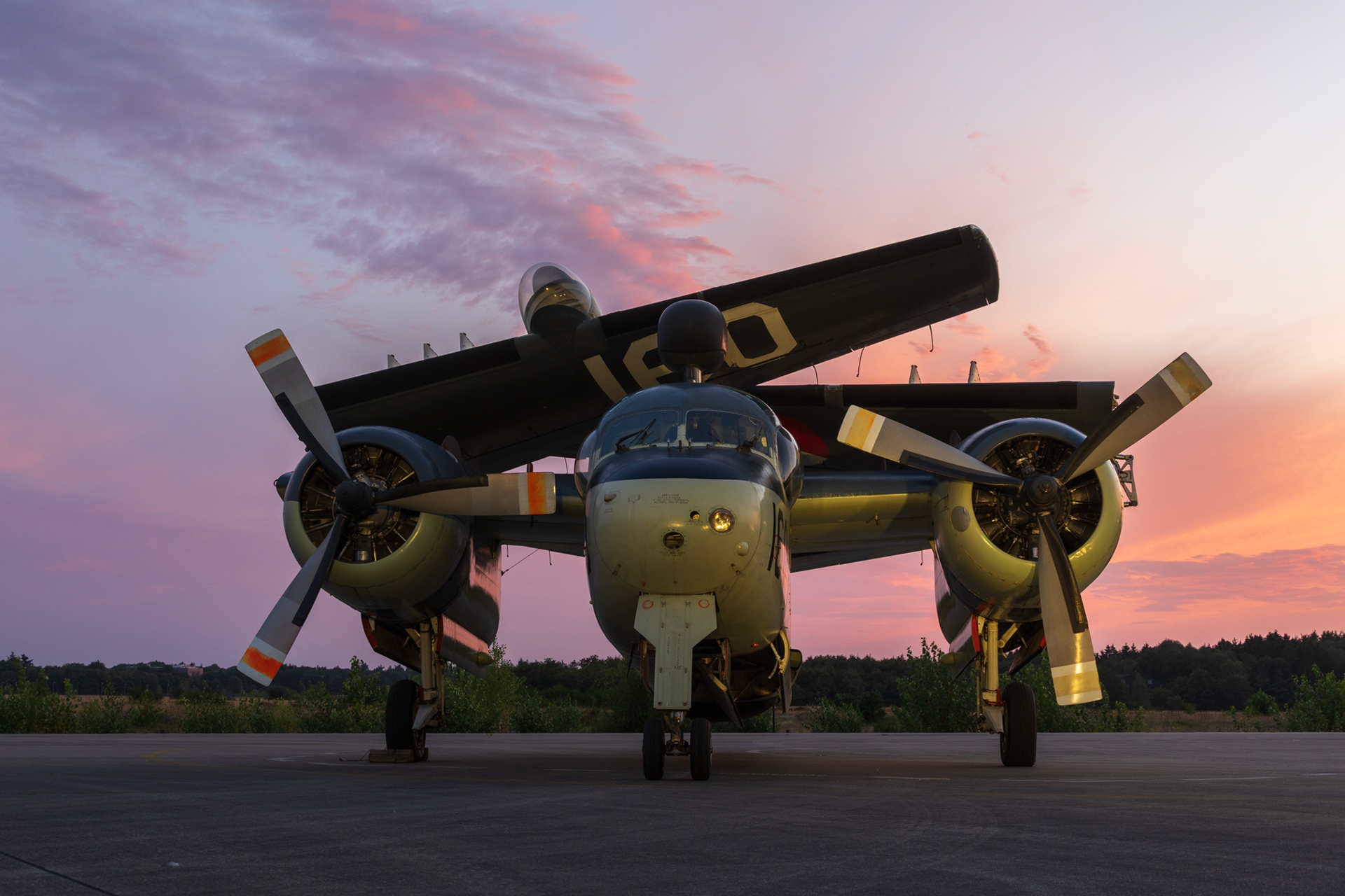 Een Grumman Tracker met gevouwen vleugels tijdens een kleurrijke zonsondergang