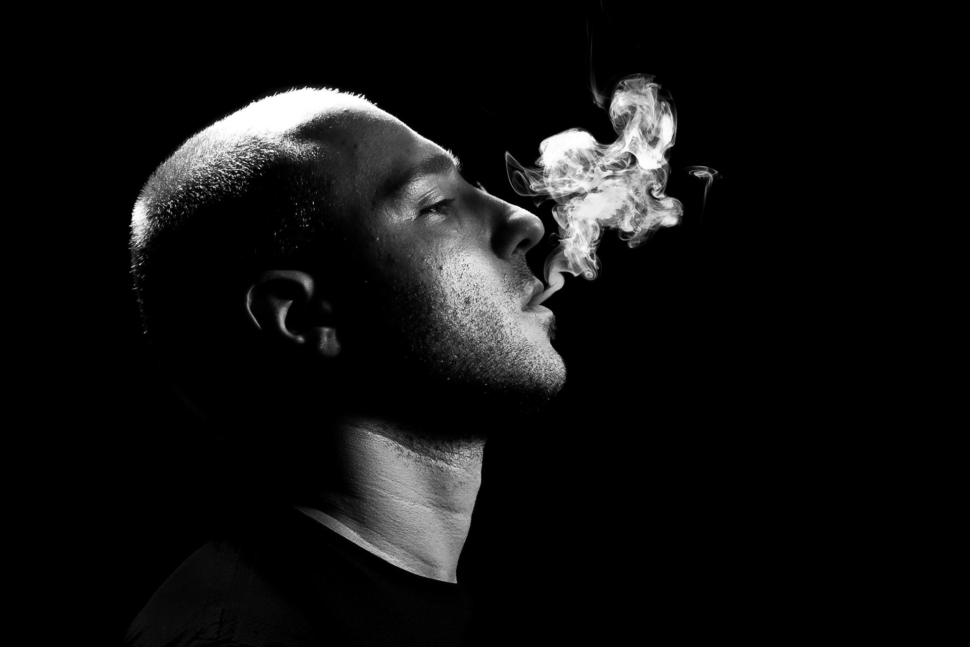 A young man smoking on a black background, Copyspace on right