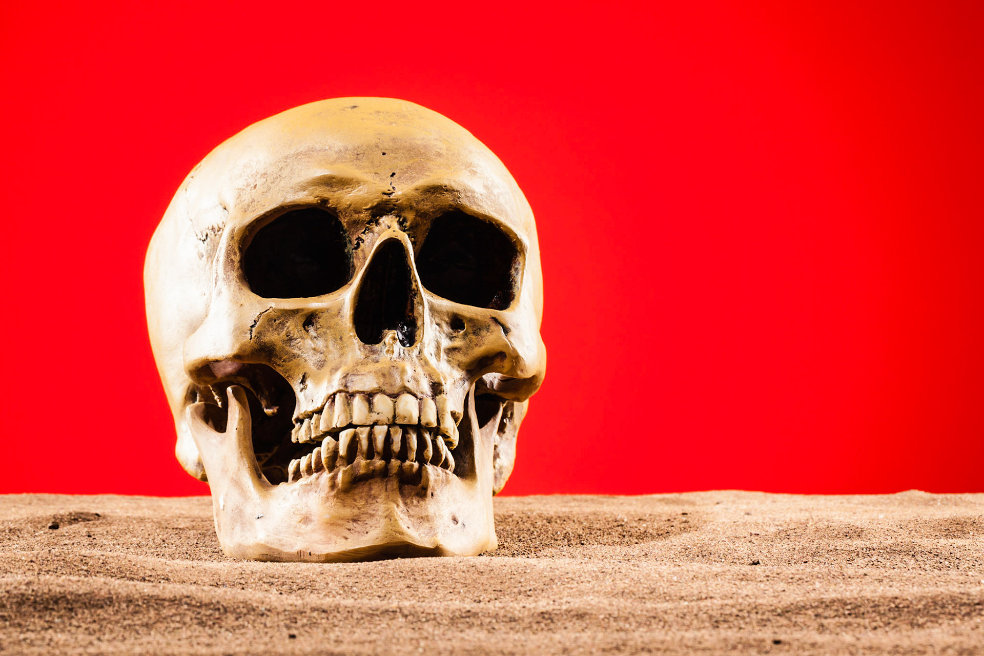 A human skull lying on the sand with a red post-apocalyptic sky as background. Could be a metaphore for global warming or hell.