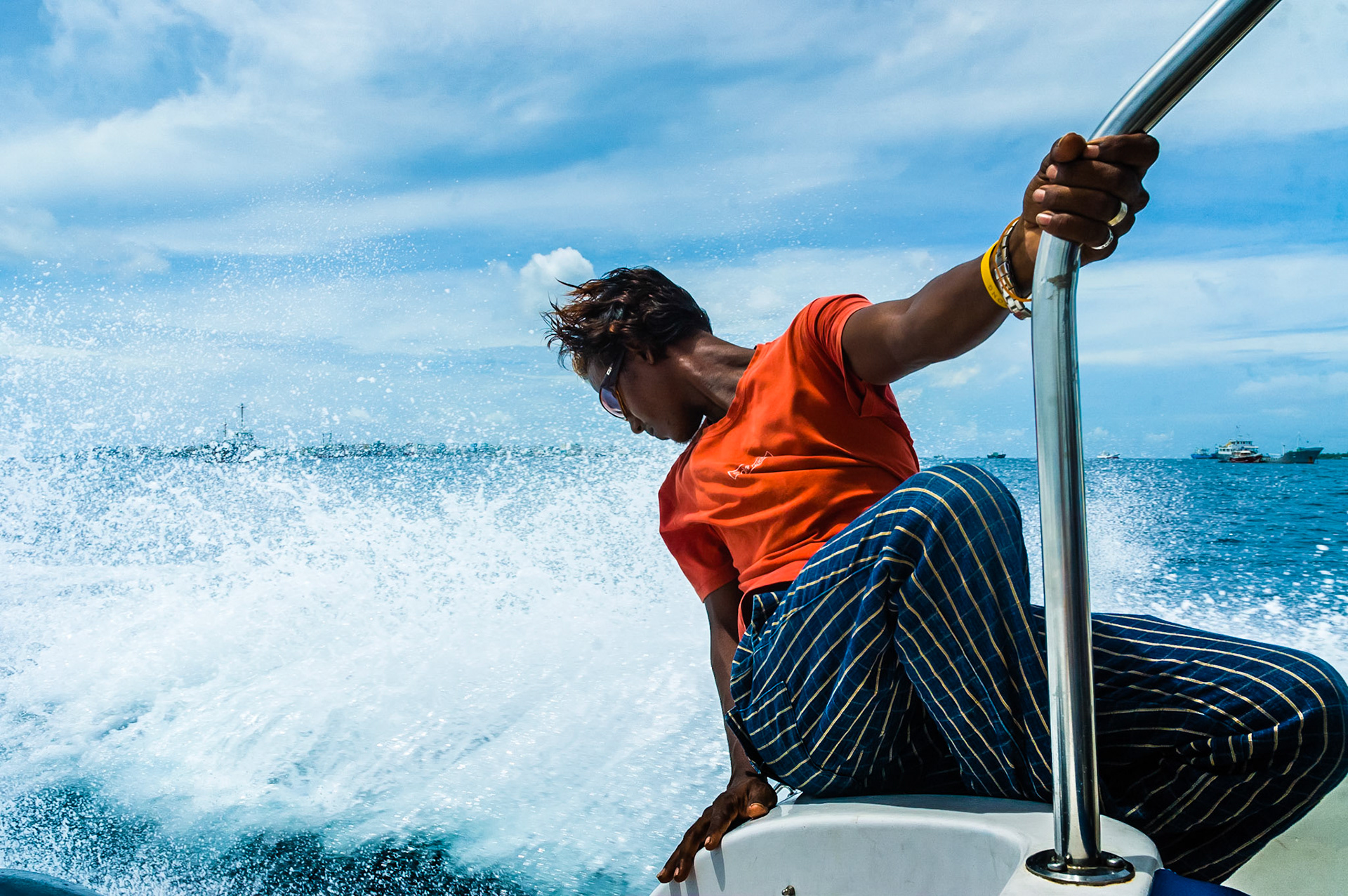 A man sitting on the back of a motorized boat looking at the trail in the sea