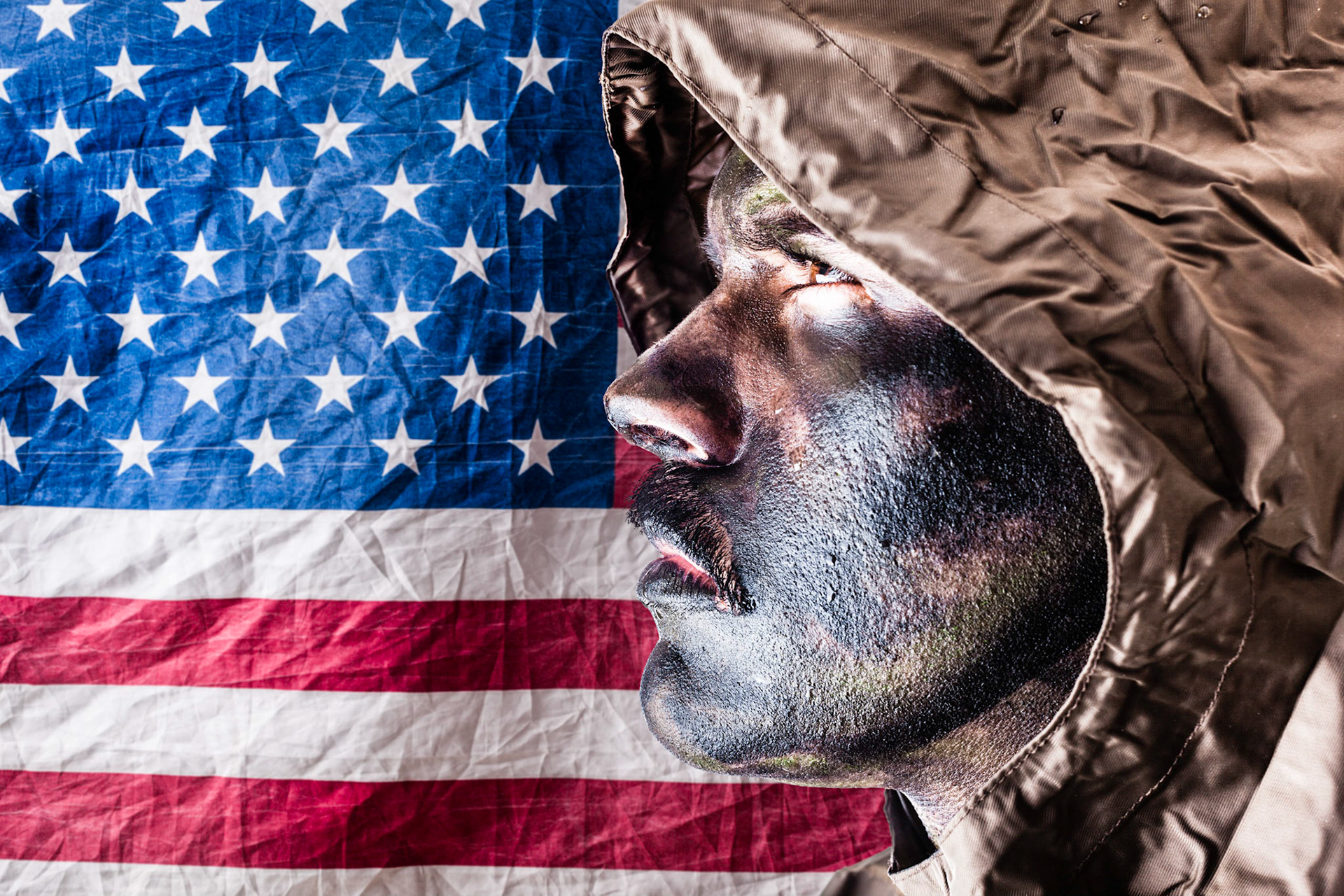 a soldier wearing a poncho or raincoat and army camouflage face paint over the american flag