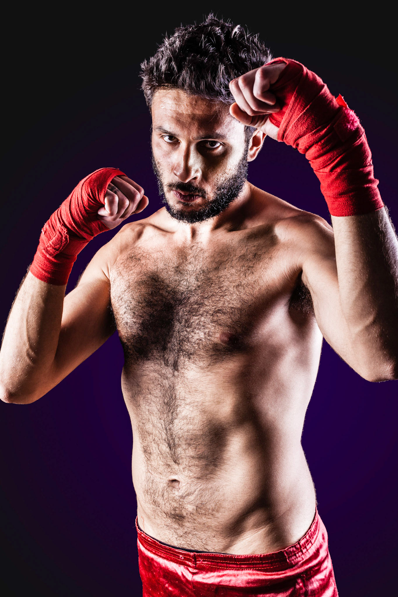 a very muscular young boxer with red trunks and hand wraps over a dark background
