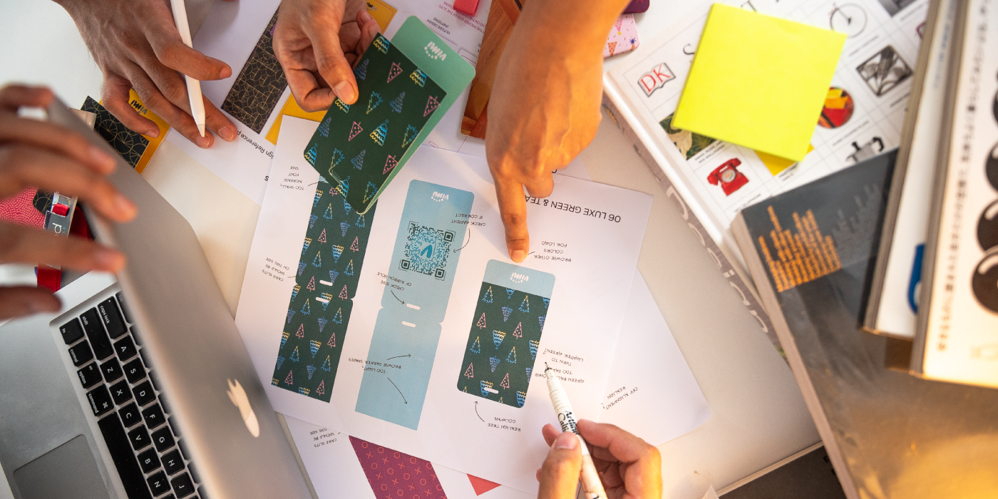 creative shot of desk with laptop, colorful designs of git tags and hands of designers ideating, with design books