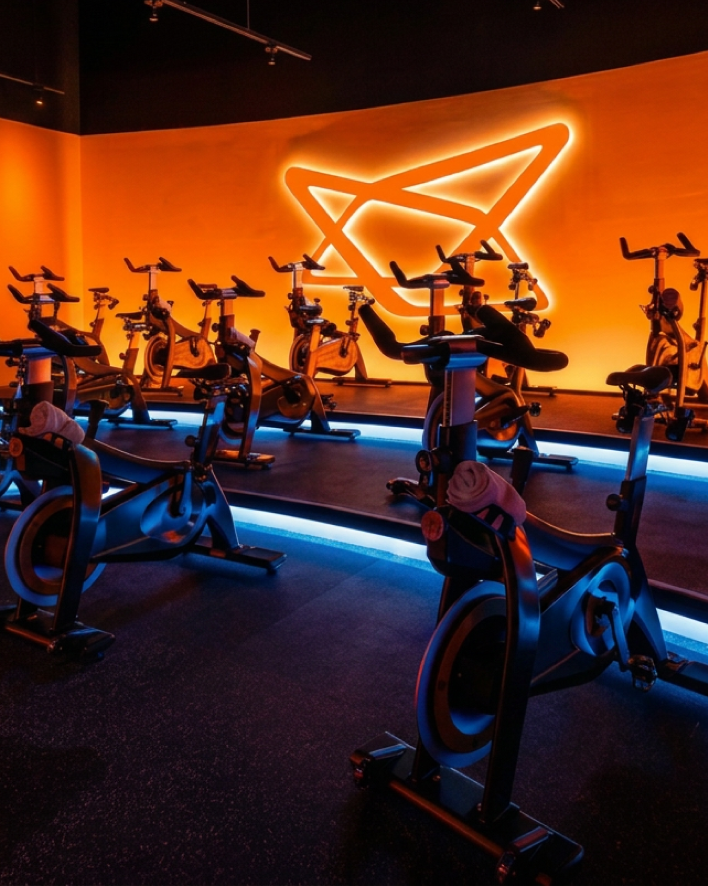 orange and blue lit indoor cycling studio with stationary bikes with big logo signage on the wall
