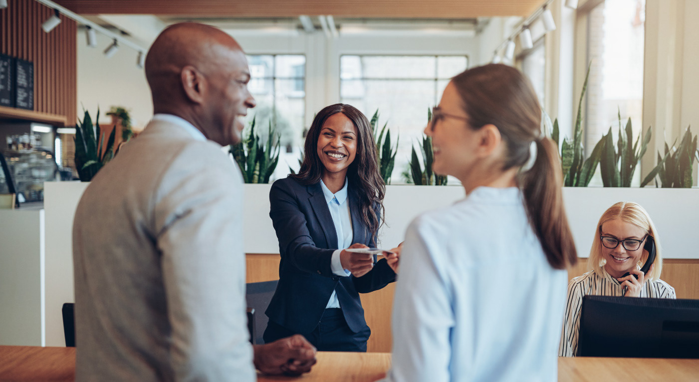 Black woman receptionist handing over a brochure to a couple in a reception lobby