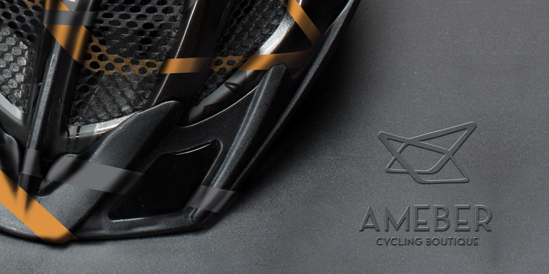 black cycling helmet zoom in detail with gray and orange stripes, embossed ameber cycling logo on the side