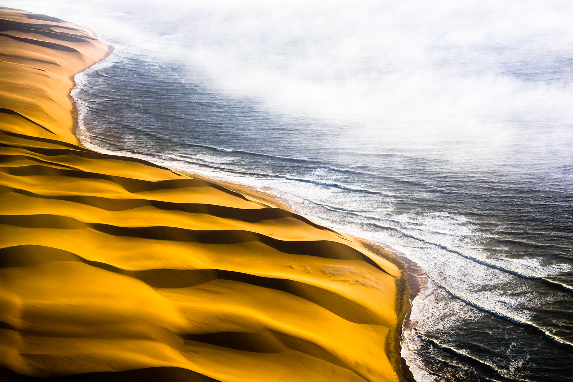 Setkání živlů na jihozápadním pobřeží Afriky. Rozpálená poušť padající přímo do studeného oceánu, k tomu časté mlhy a silný vítr. To je recept na opravdu nehostinné pobřeží, kterému se ne nadarmo přezdívá Pobřeží koster. Zbytky tuleňů, rezivějící vraky lodí, jež si postupně bere pod svá křídla písek, ale i lidské ostatky, které naopak odhaluje prudký vítr naznačují, odkud název Skeleton Coast pochází.