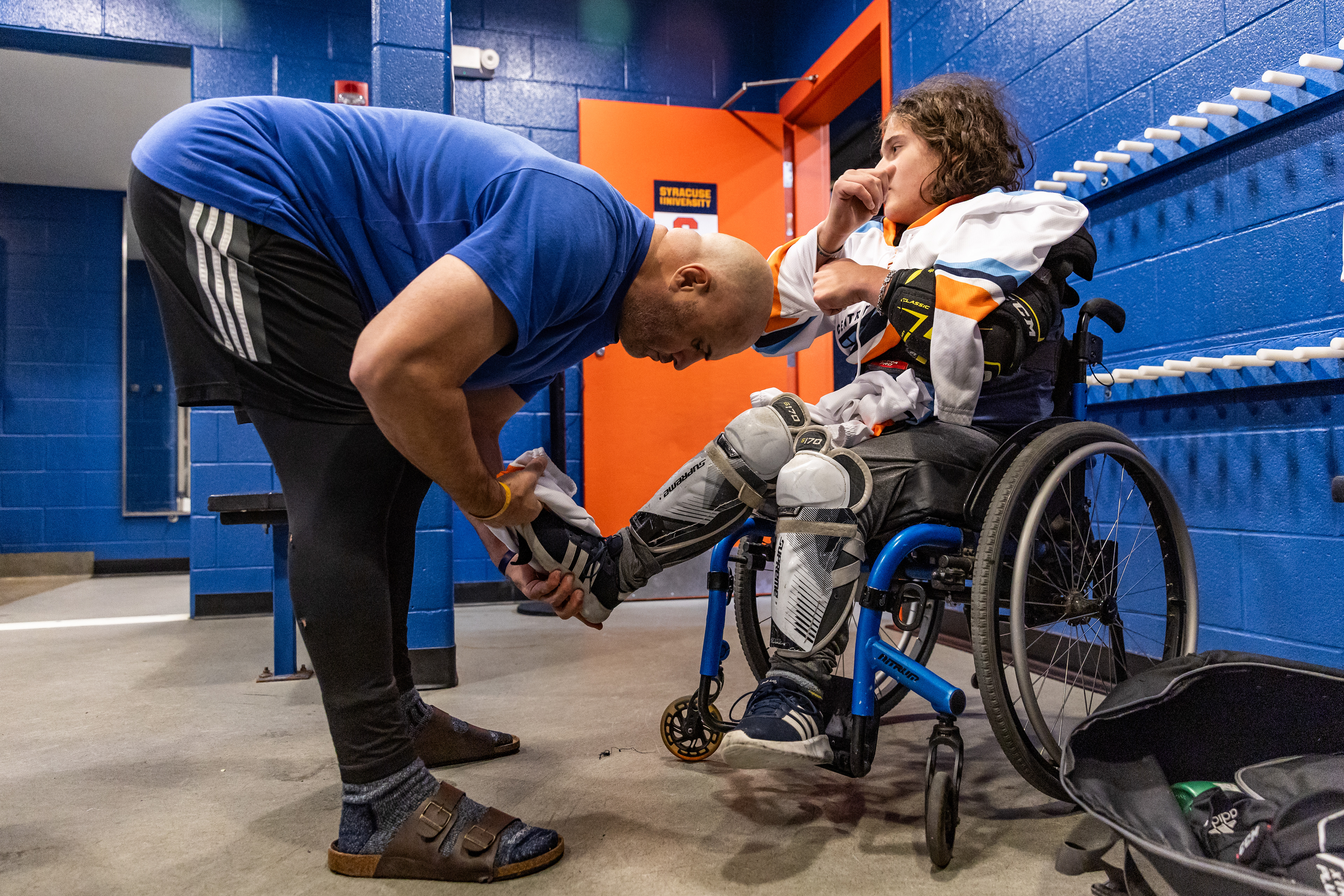 Jamie Favata helps his son, Myles Favata, put on his gear before their charity game against the Syracuse men’s club hockey team.  Myles fell in love with hockey at age three while watching a game on TV with his dad. After watching the Paralympics in 2018, eight-year-old Myles knew he wanted to be on the ice, not just watch from the sidelines.  Before becoming a father, Jamie promised to do everything he could to support his children’s sports aspirations. Finding the Central New York Flyers is just one way Jamie has helped turn Myles’ dreams into a reality.