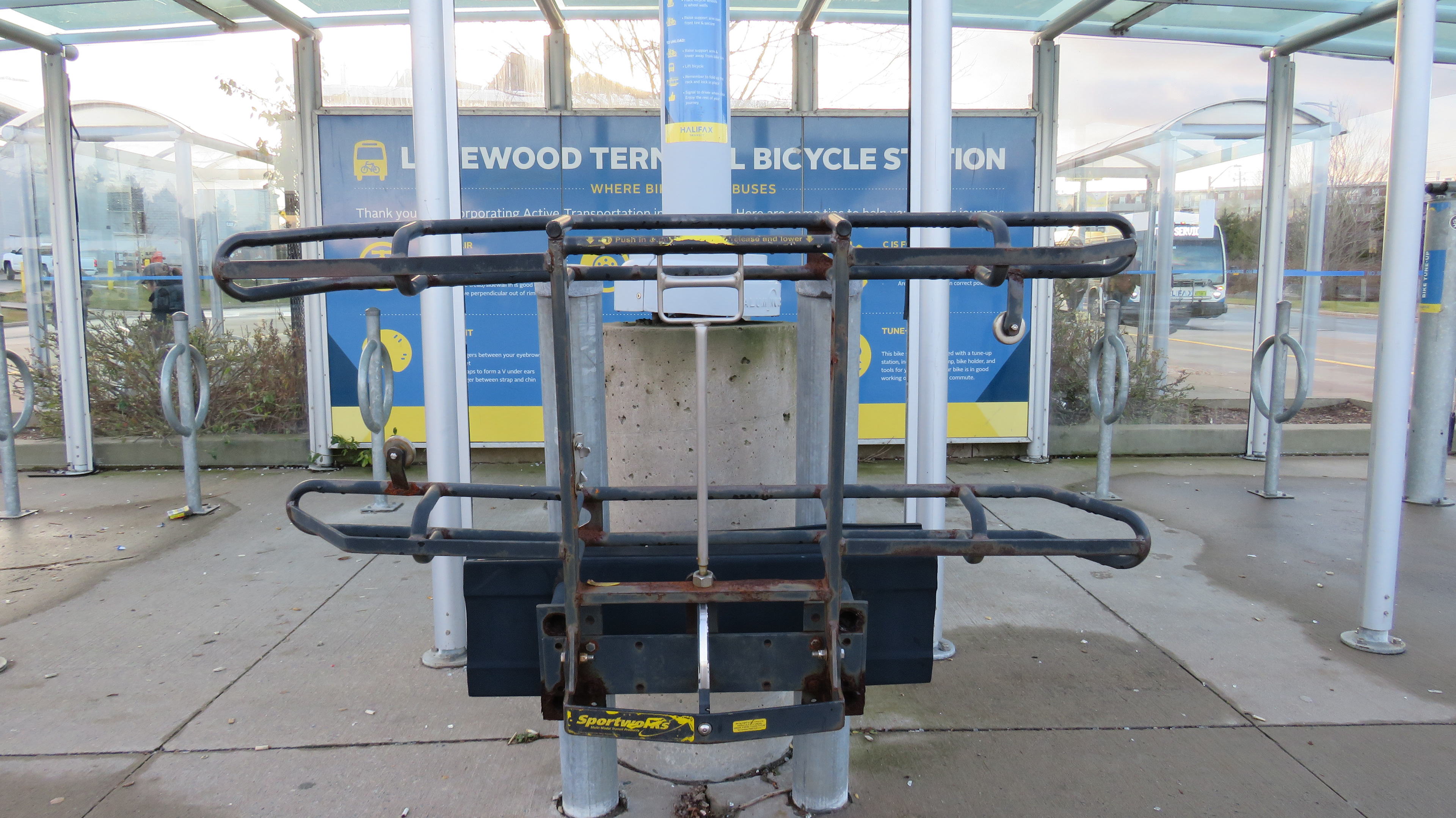 Halifax Transit is interested in having more people use their bus bike racks. This practice rack is installed at Lacewood terminal for people to test the racks before they have to board the bus. The pole behind it has basic instructions on how to use the bike rack demo station. Behind the bike rack demo is a sign educating people on basic safety checks and tools for cyclists to do quick bike repairs. In comparison to the safety sign behind it, the Bike rack instructions are easy to miss. 