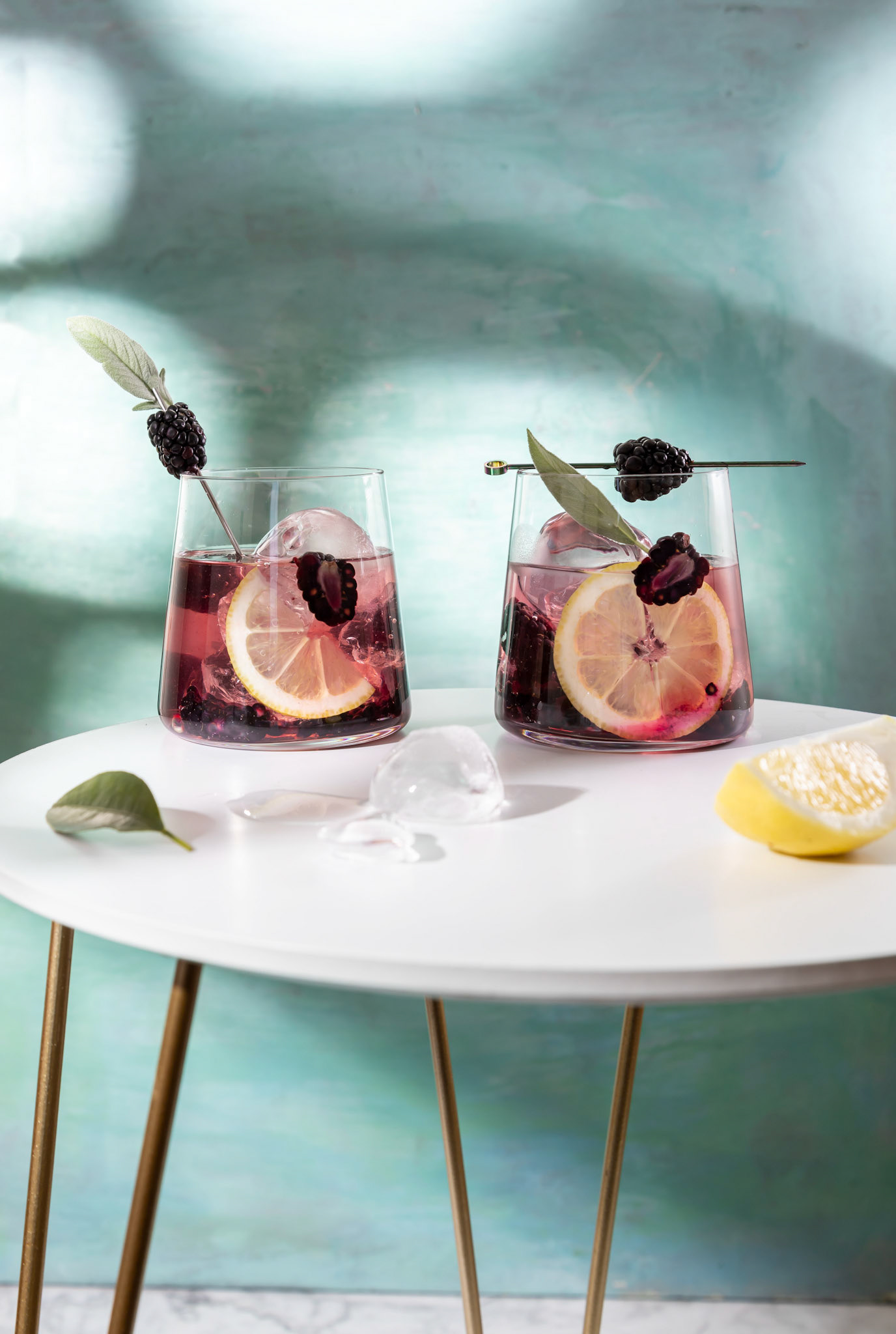 Blackberry cocktail . Berry cocktails in glass with ice and lemon on the white table .