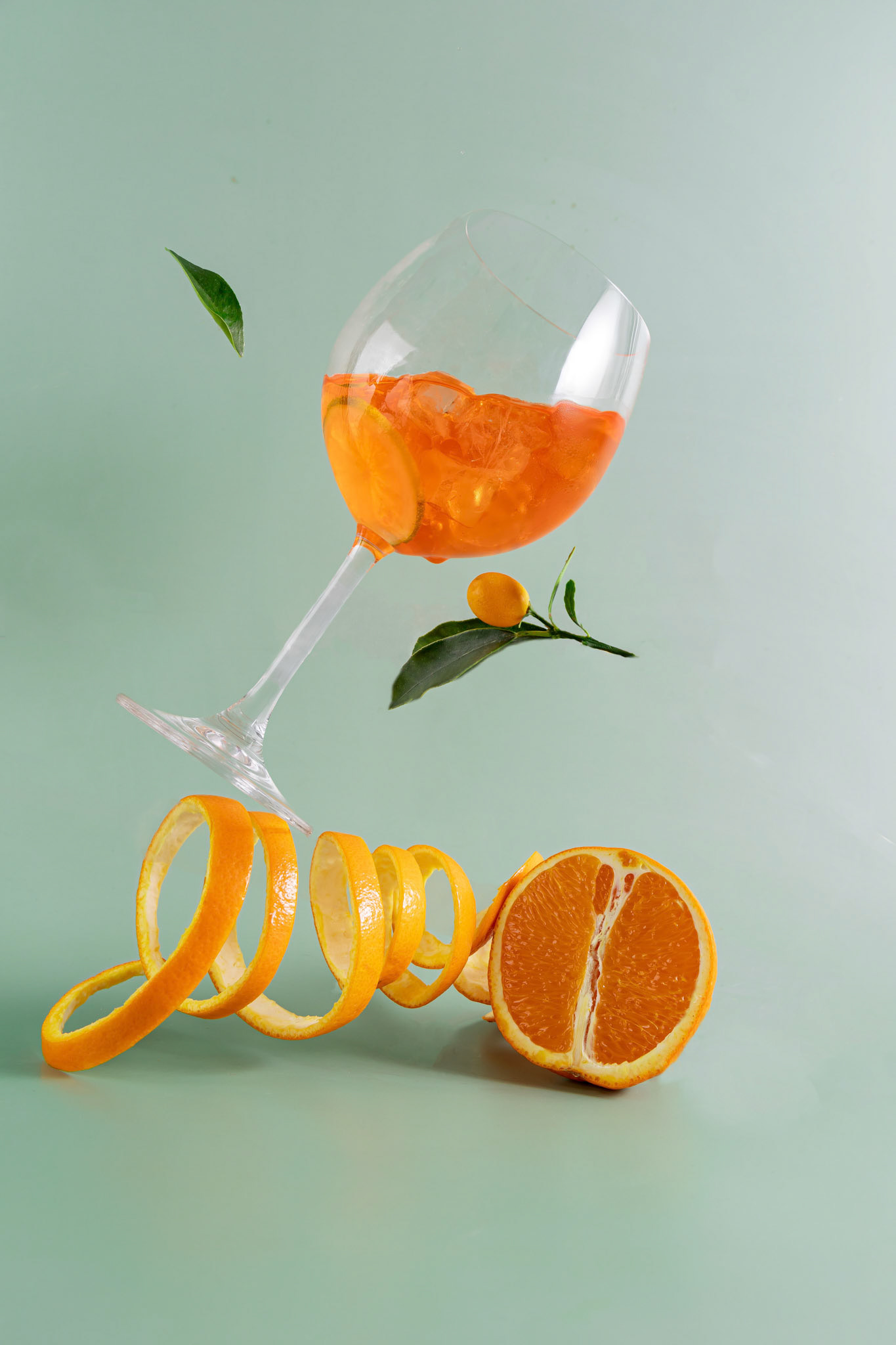 Glass of aperol spritz cocktail, with orange peel, photo with a balancing object on a green background .