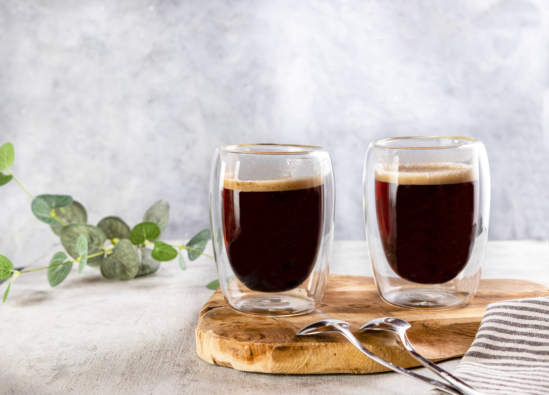 A glass double-sided cups of coffee with coffee in it on a wooden board on a grey background .