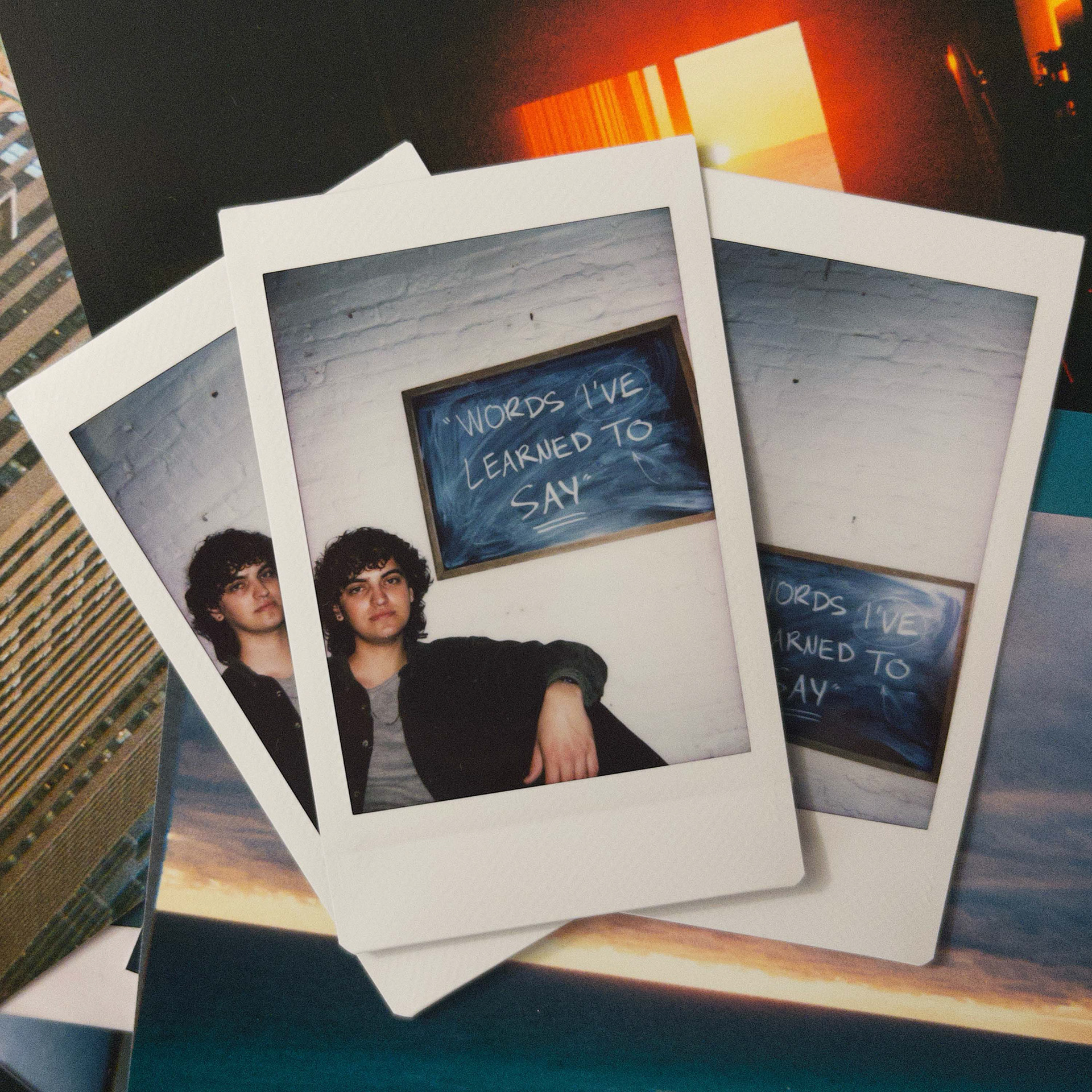 album cover for "Words I've Learned to Say" by Thomas Allain featuring three stacked polaroids of thomas in front of a chalkboard reading "words I've learned to say"