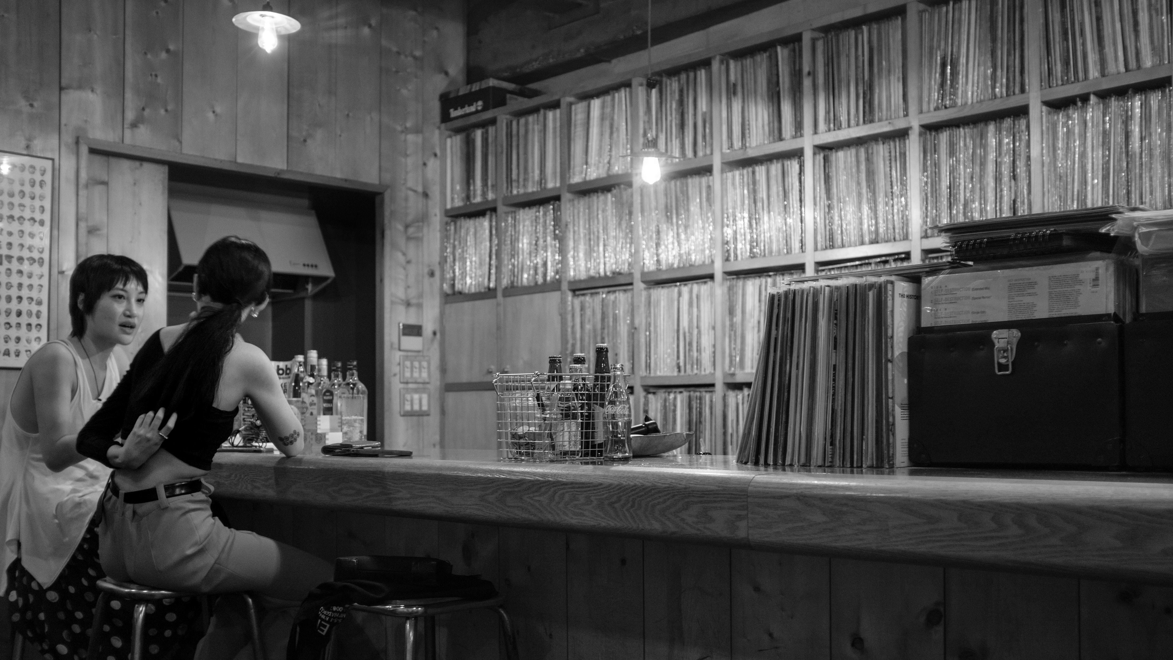 Captured by Ikeji Uju: Two women sitting at the counter of a vinyl bar in Shibuya City, Tokyo, Japan. Shot in Black and White.