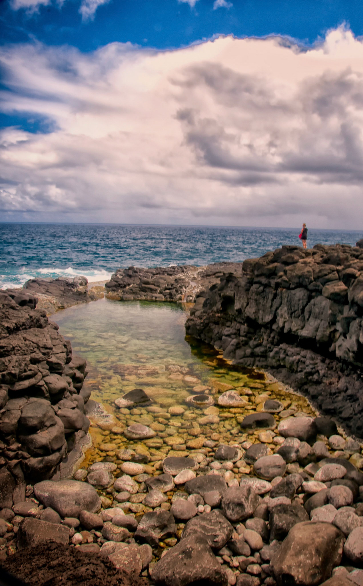 Woman in solitude, gazing at the ocean overlooking Queens Bath on the island of  Kauai, Hawaii, USA
