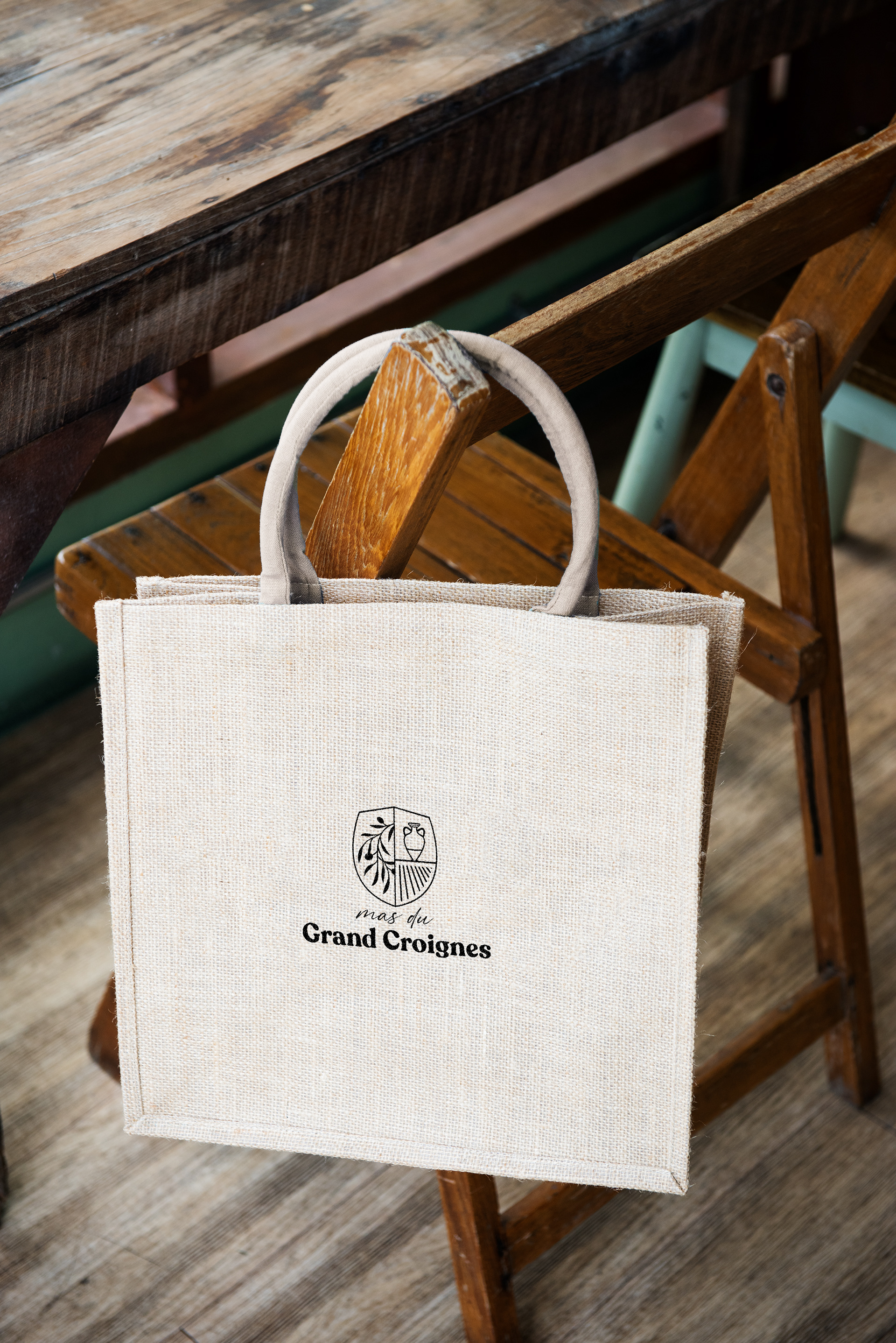 Un tote bag brodé avec le logo du Mas du Grand Croignes accroché sur une chaise en bois