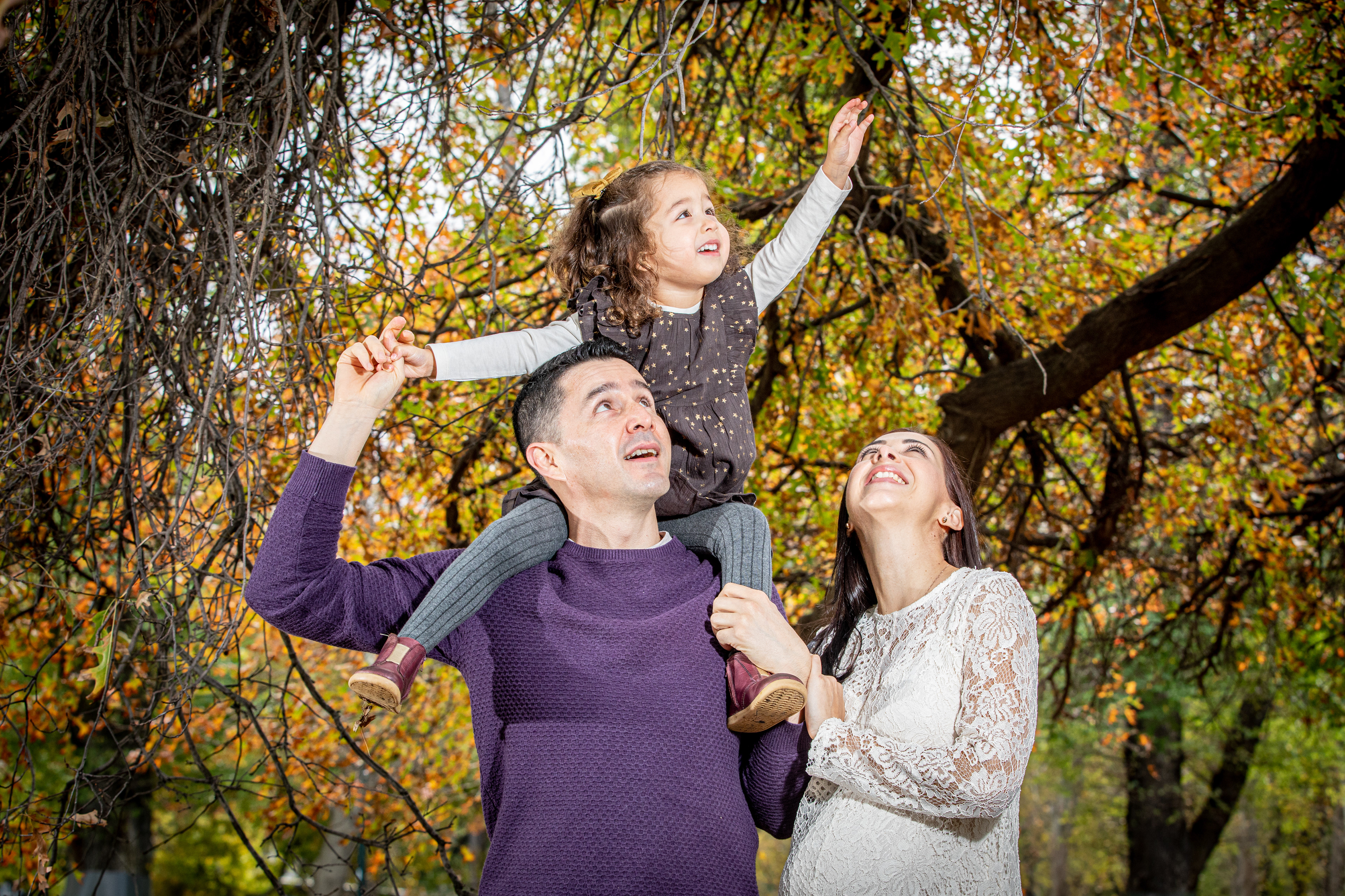 Child sitting on a parent’s shoulders beneath autumn trees