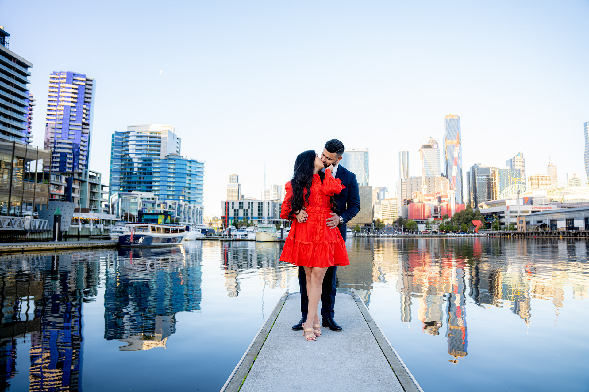 Couple standing beside the waterfront with city buildings reflected behind