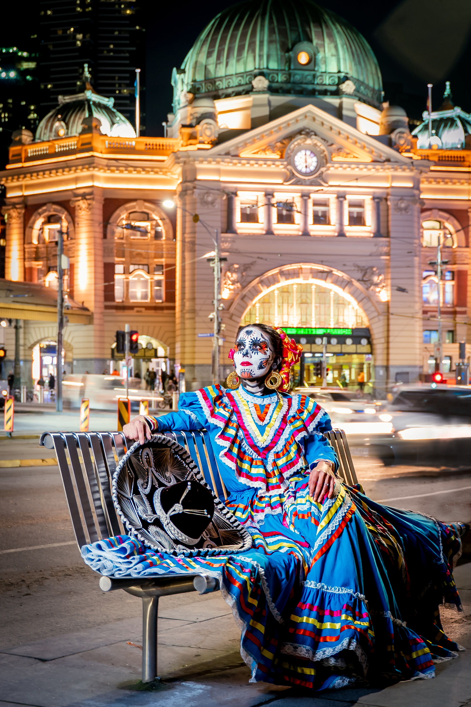 Portrait in a colourful dress and skull face paint outside Flinders Street Station at night