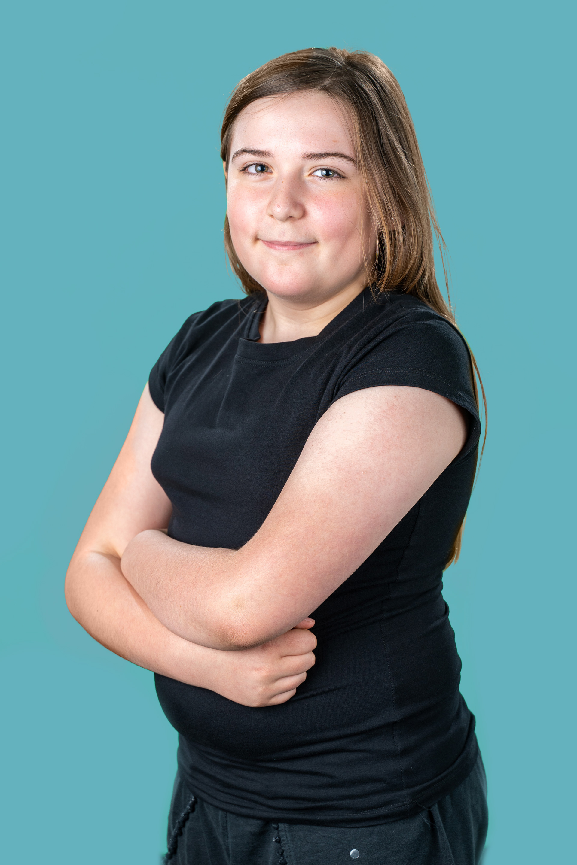 Portrait in a black top with arms folded against blue