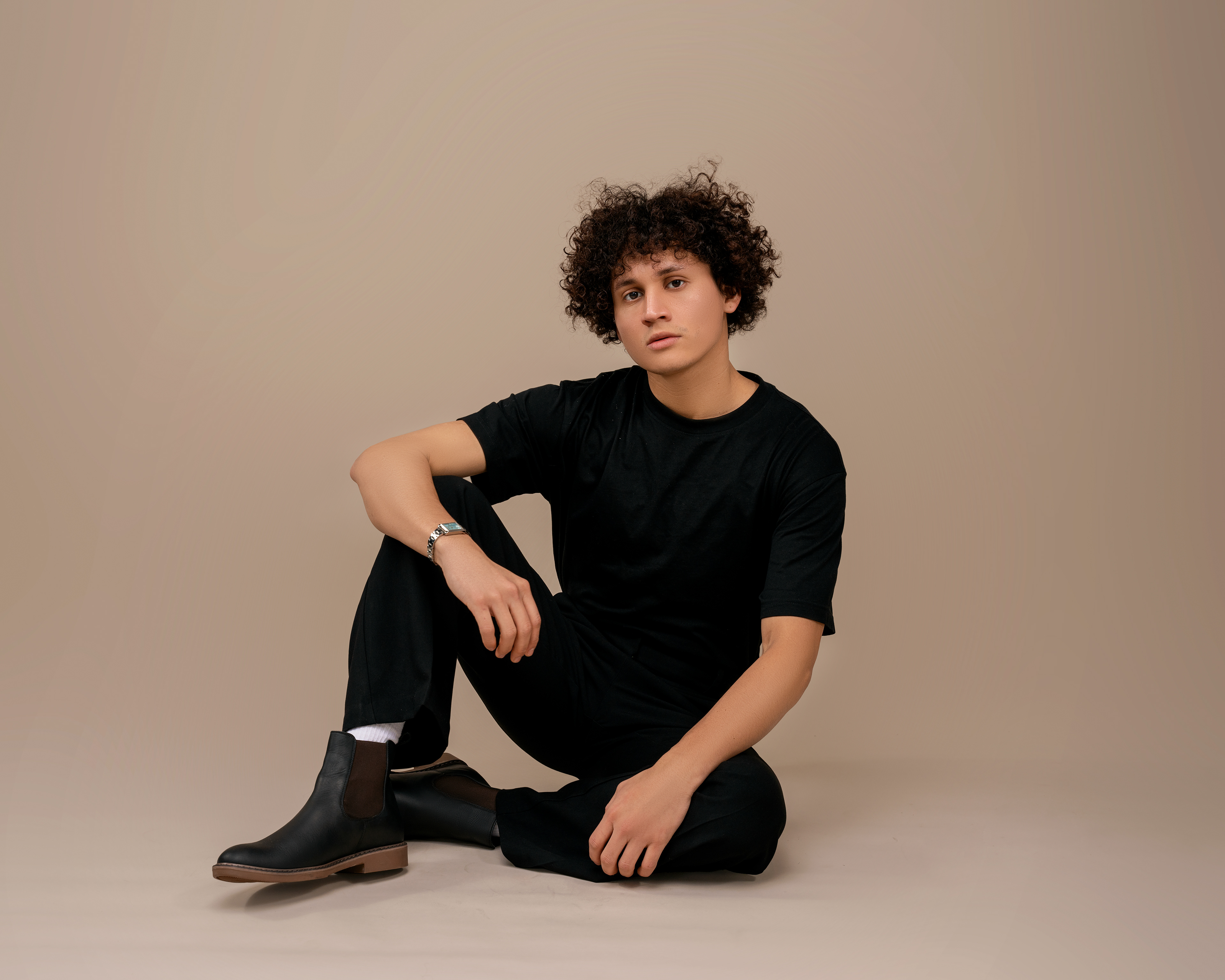 Seated portrait in black with curly hair against a neutral backdrop