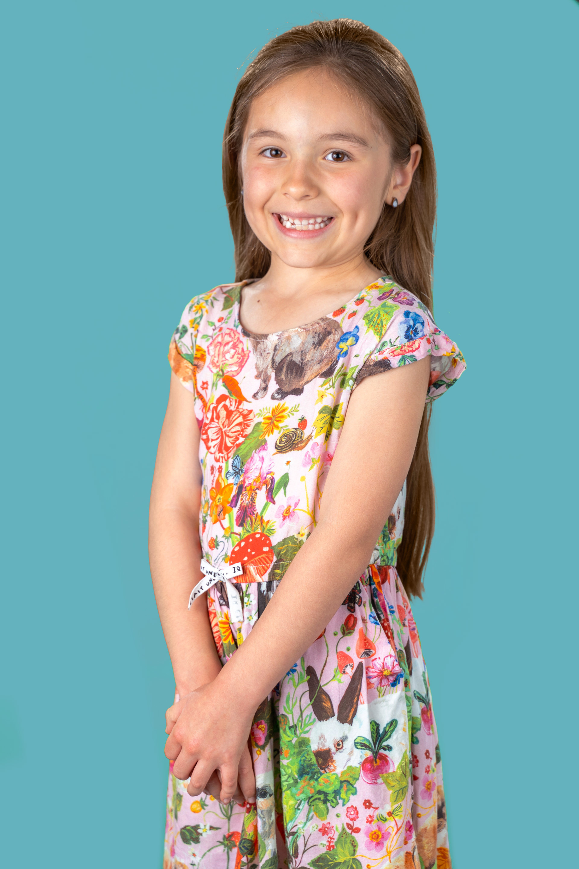 Child smiling in a floral dress against a grey background