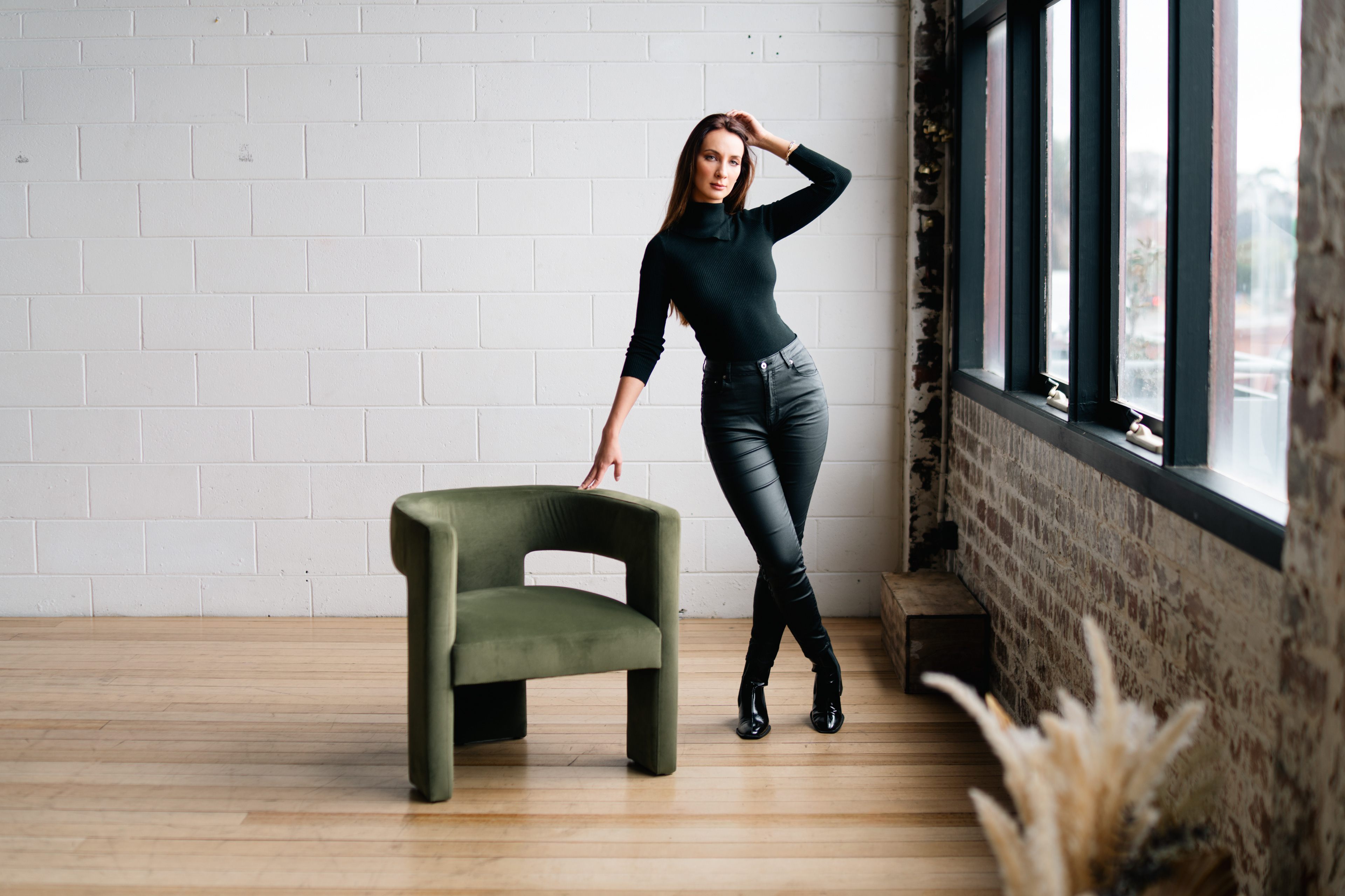 Portrait in a black outfit beside a green chair and studio windows
