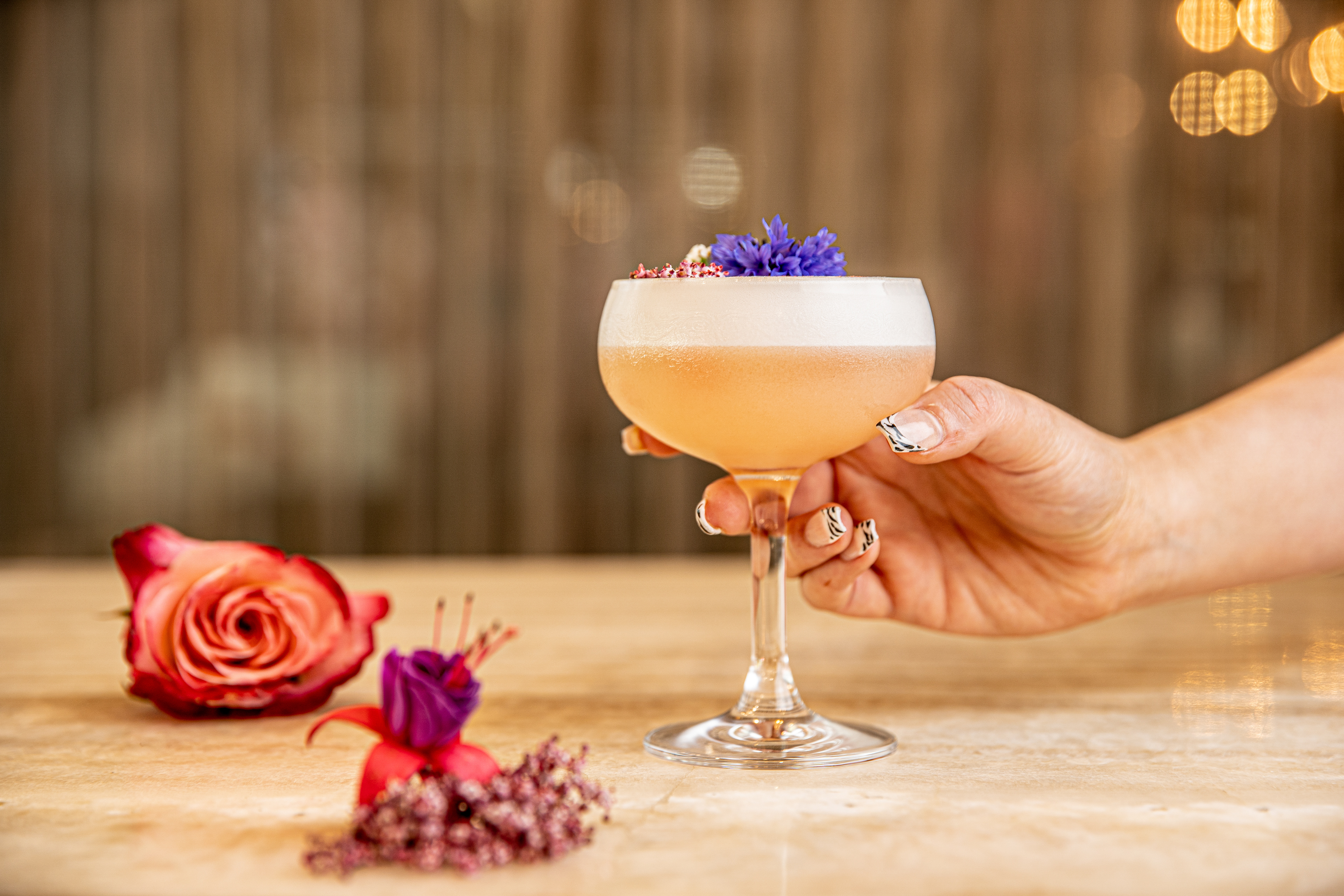 Cocktail garnished with a purple flower beside dried petals