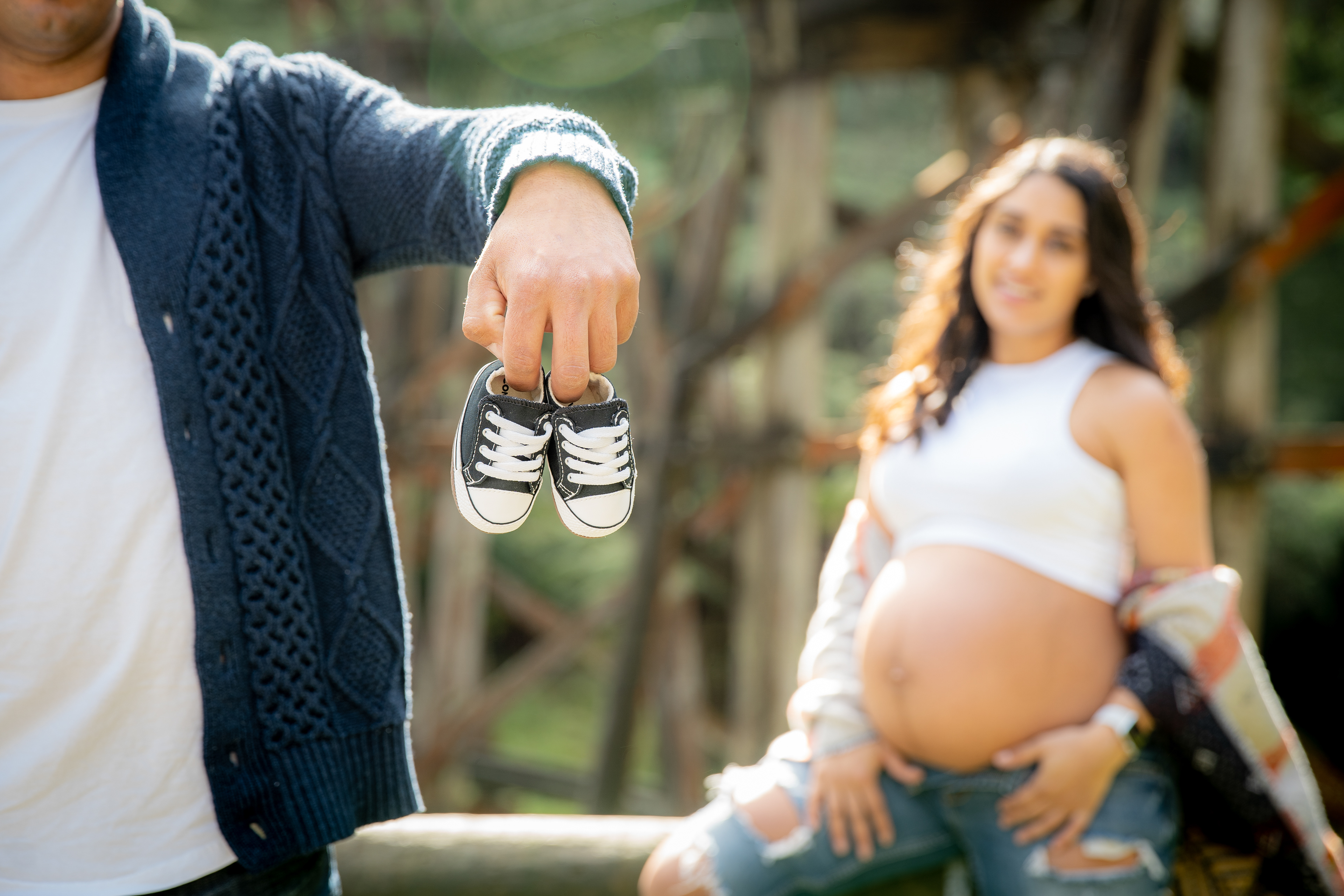 Small baby shoes held in front of an outdoor maternity portrait