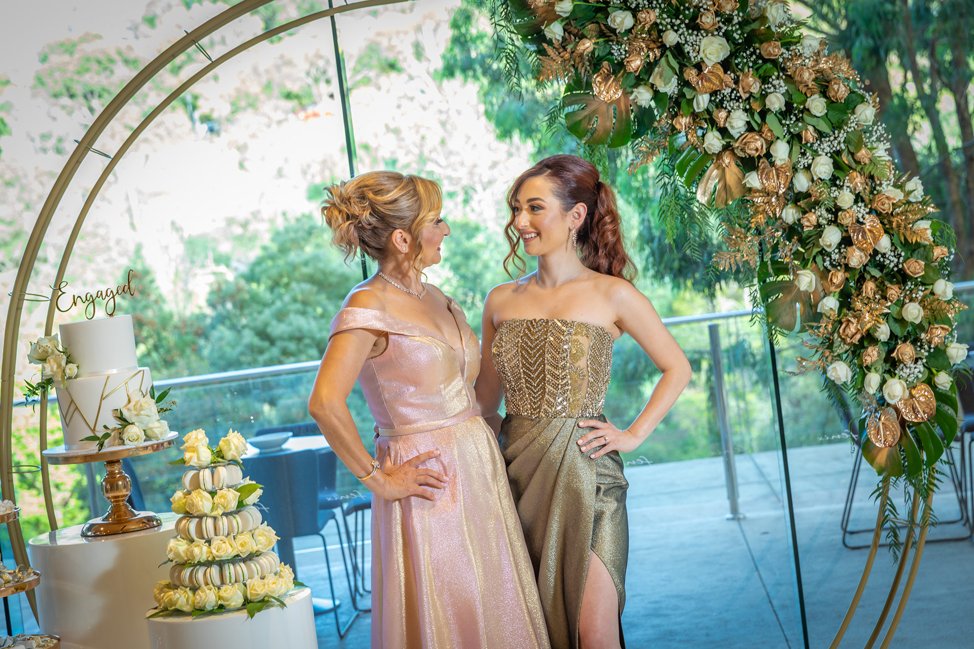 Two guests in evening dresses beside a floral backdrop