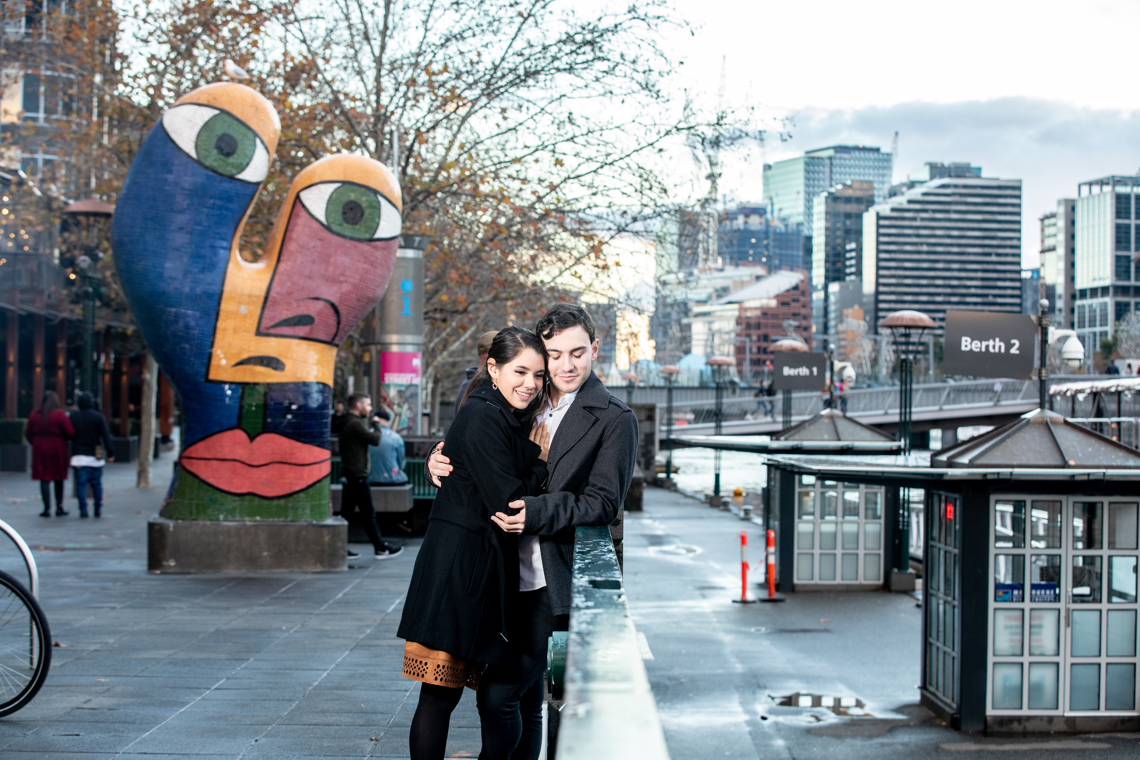 Couple posing beside colourful sculptures and city buildings