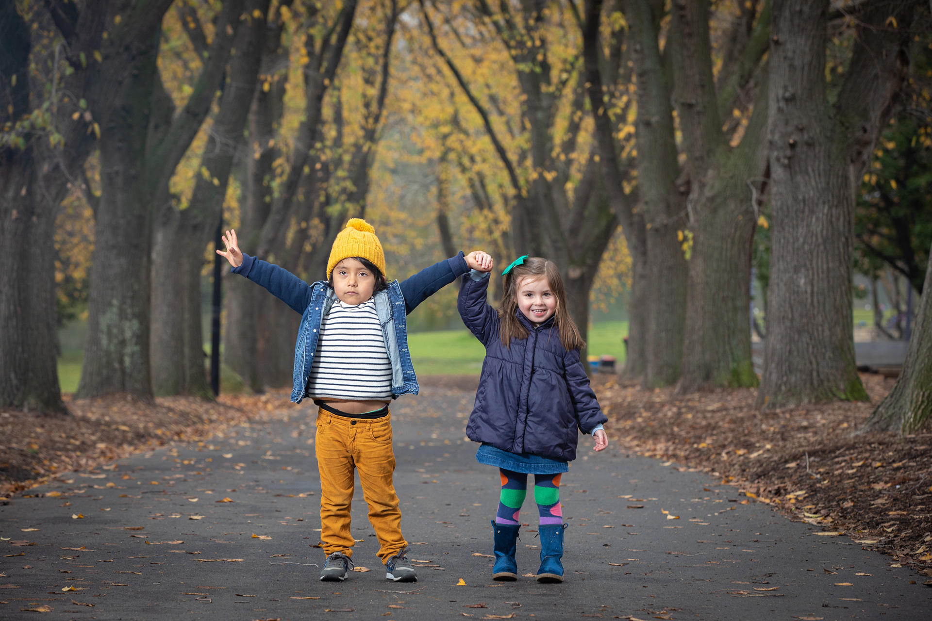 Two children standing together on a tree-lined path