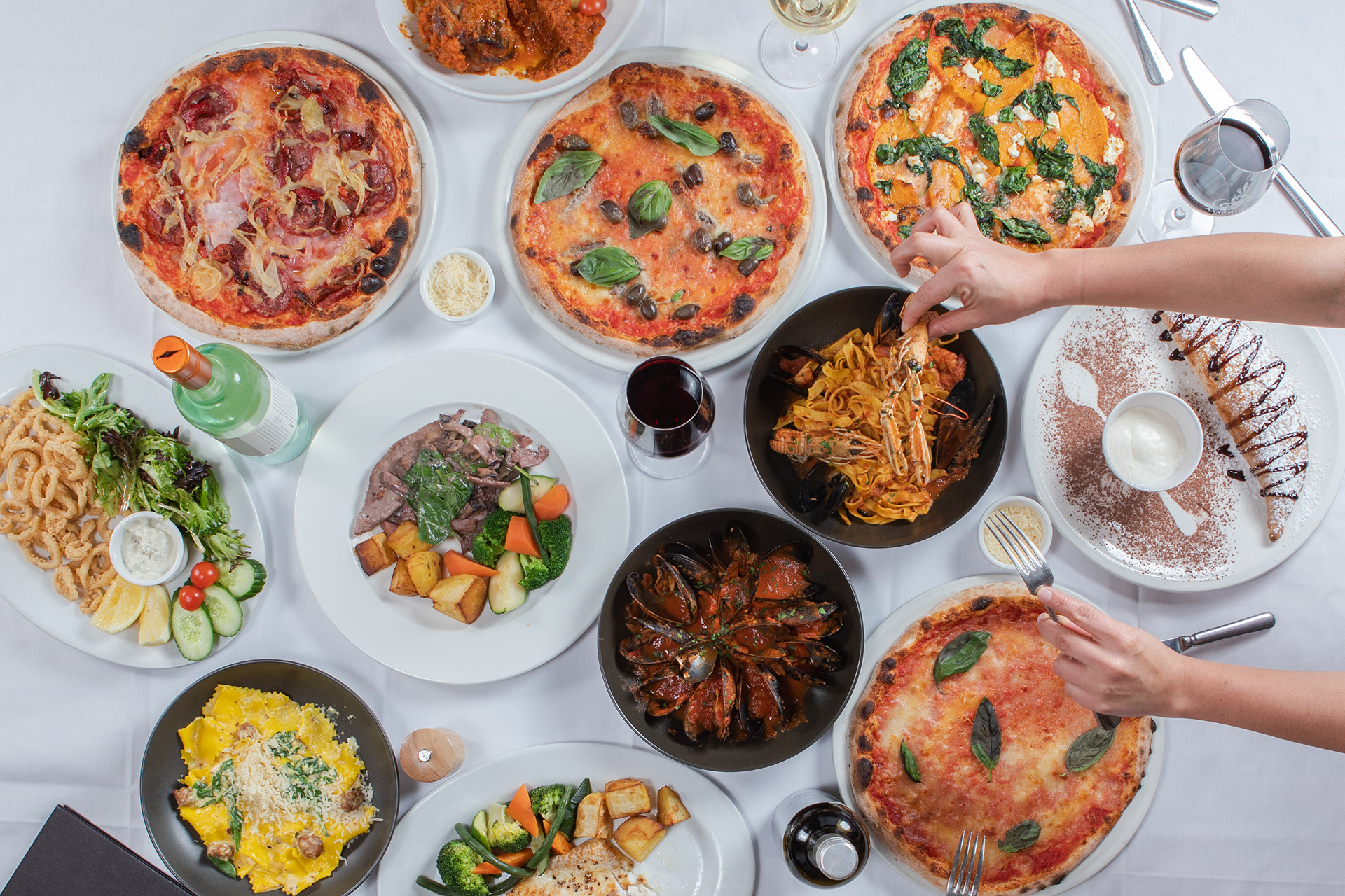 Overhead view of pizzas, salads and shared dishes