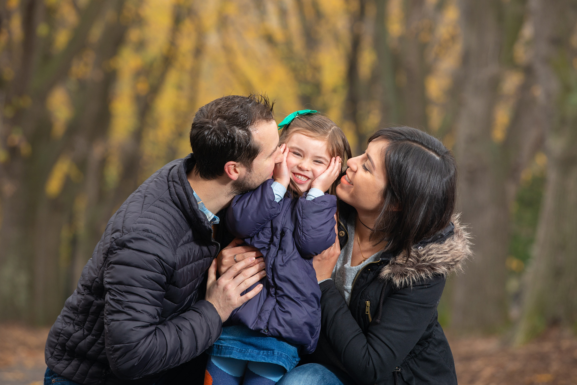 Parents kissing their child during an outdoor portrait