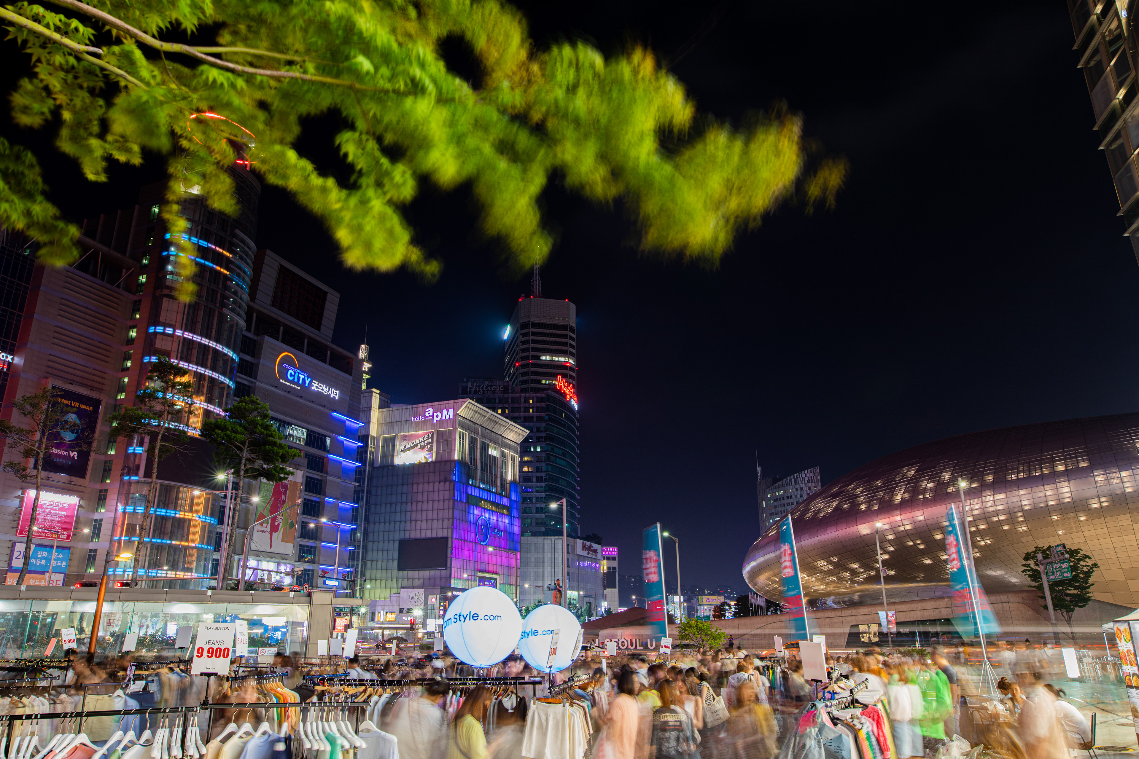 Night market beneath a tree and illuminated city buildings
