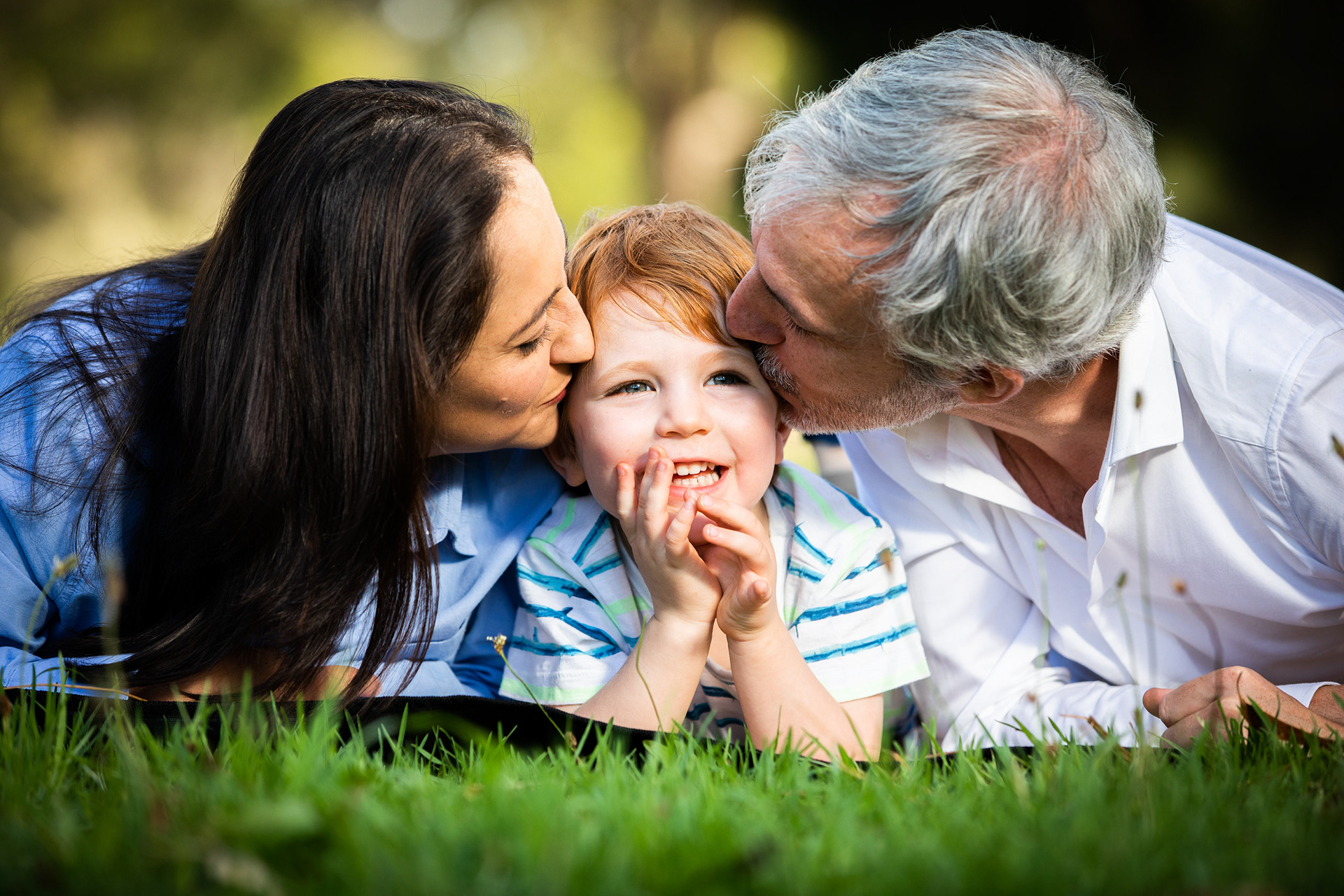 Parents kissing their child while lying on a blanket