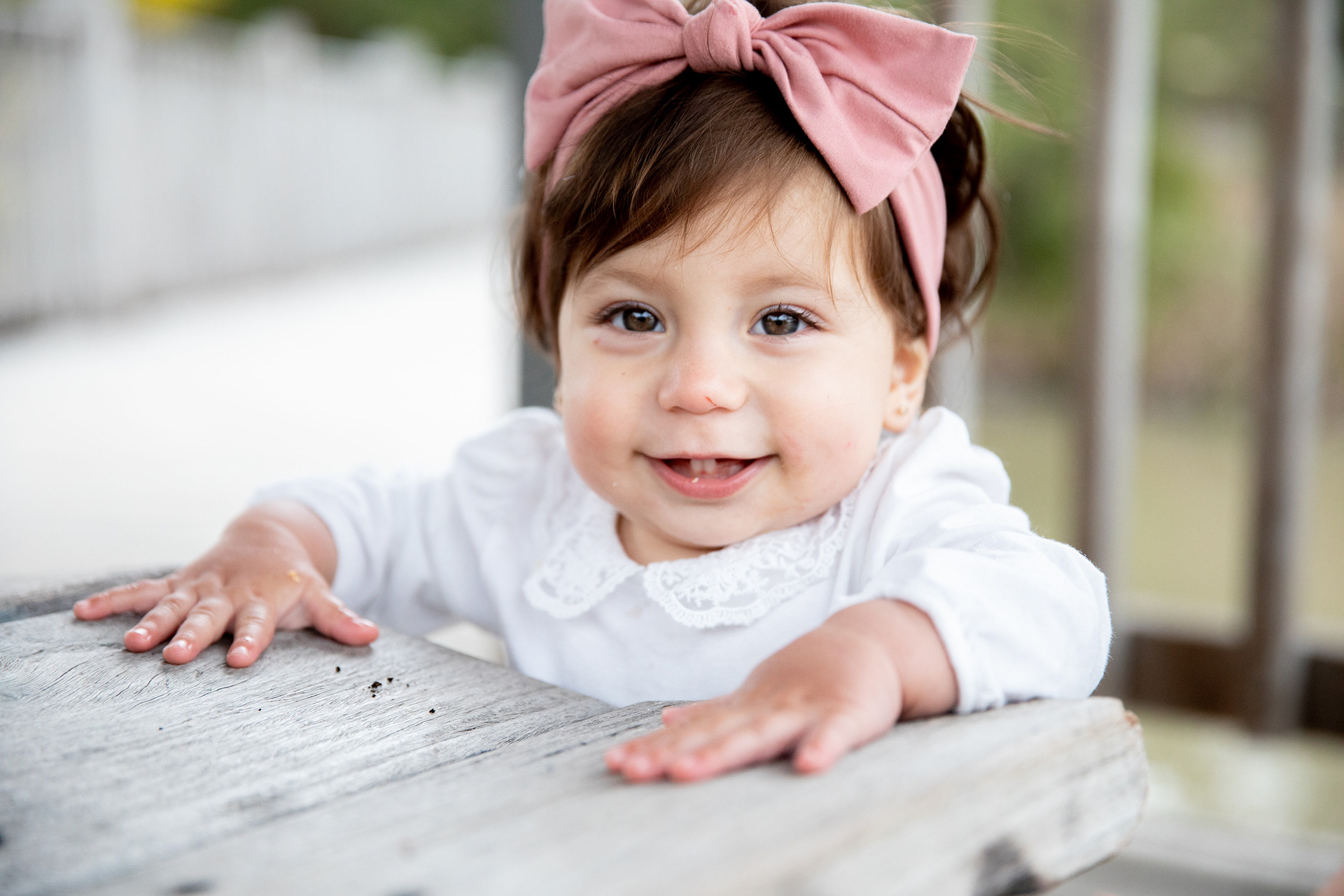 Baby wearing a pink bow beside a birthday cake