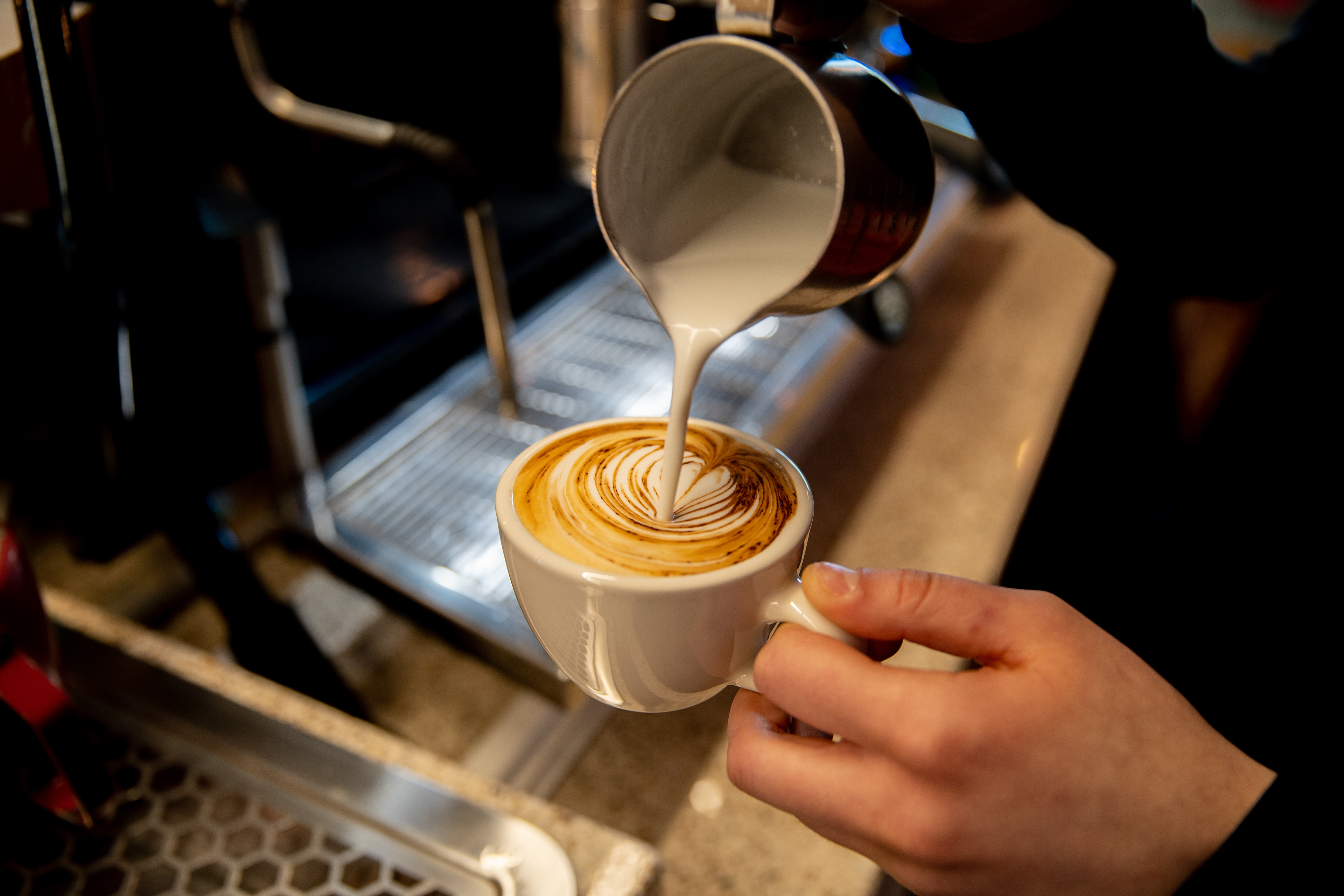 Barista pouring steamed milk into a cup of coffee
