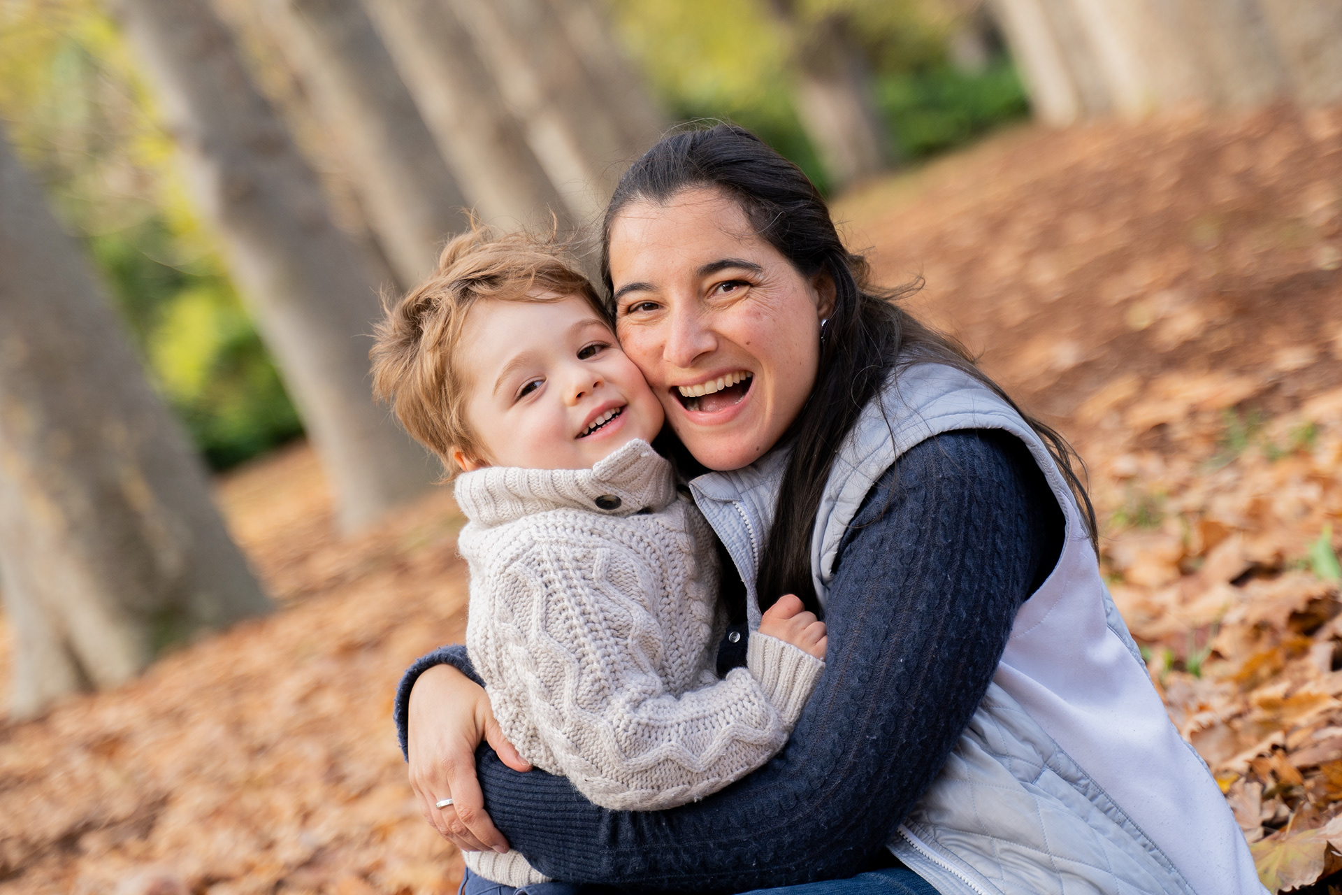 Parent cuddling a child among autumn leaves