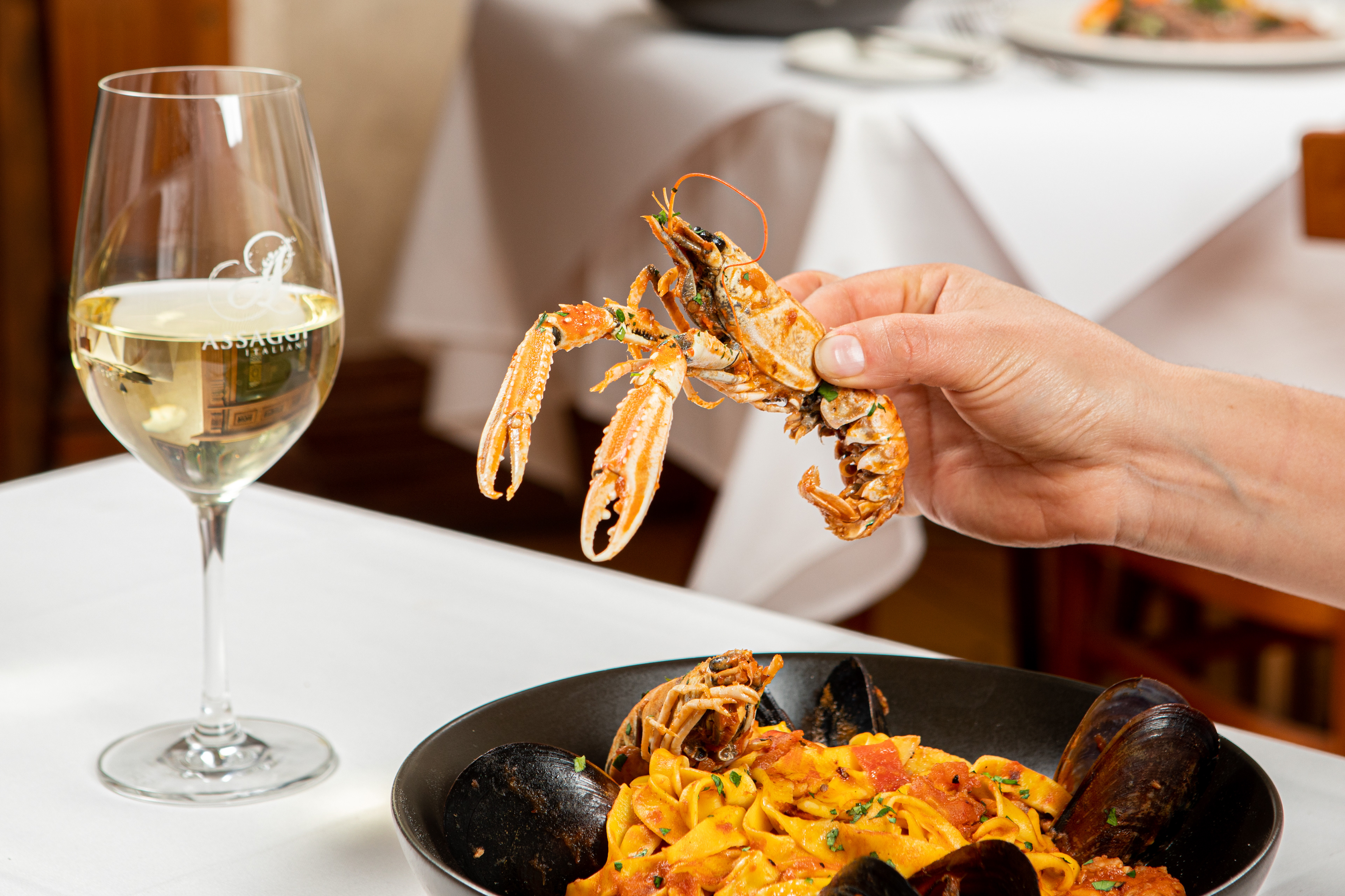 Diner lifting pasta with a fork beside a glass of white wine