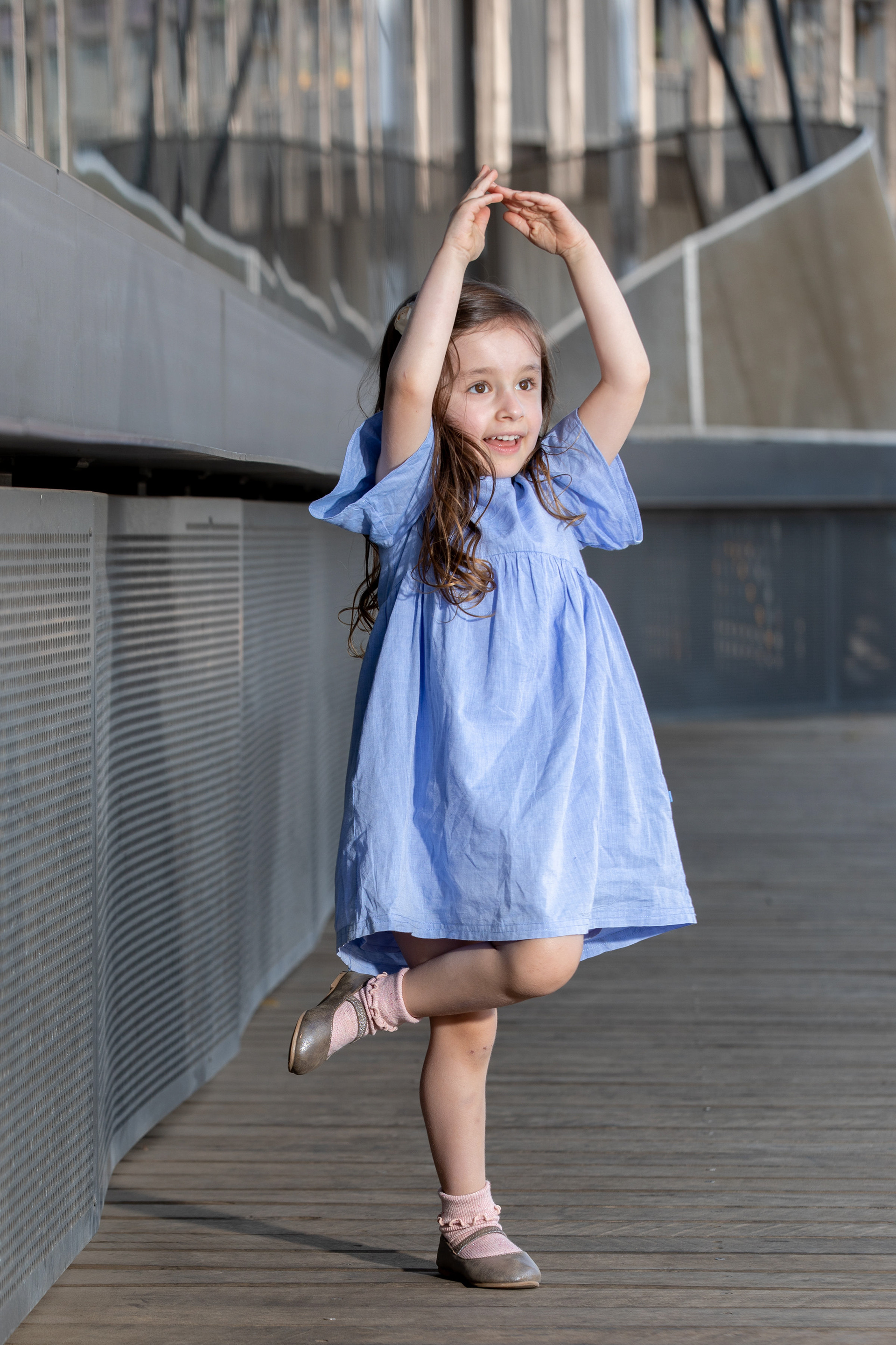 Child in a blue dress posing with arms raised