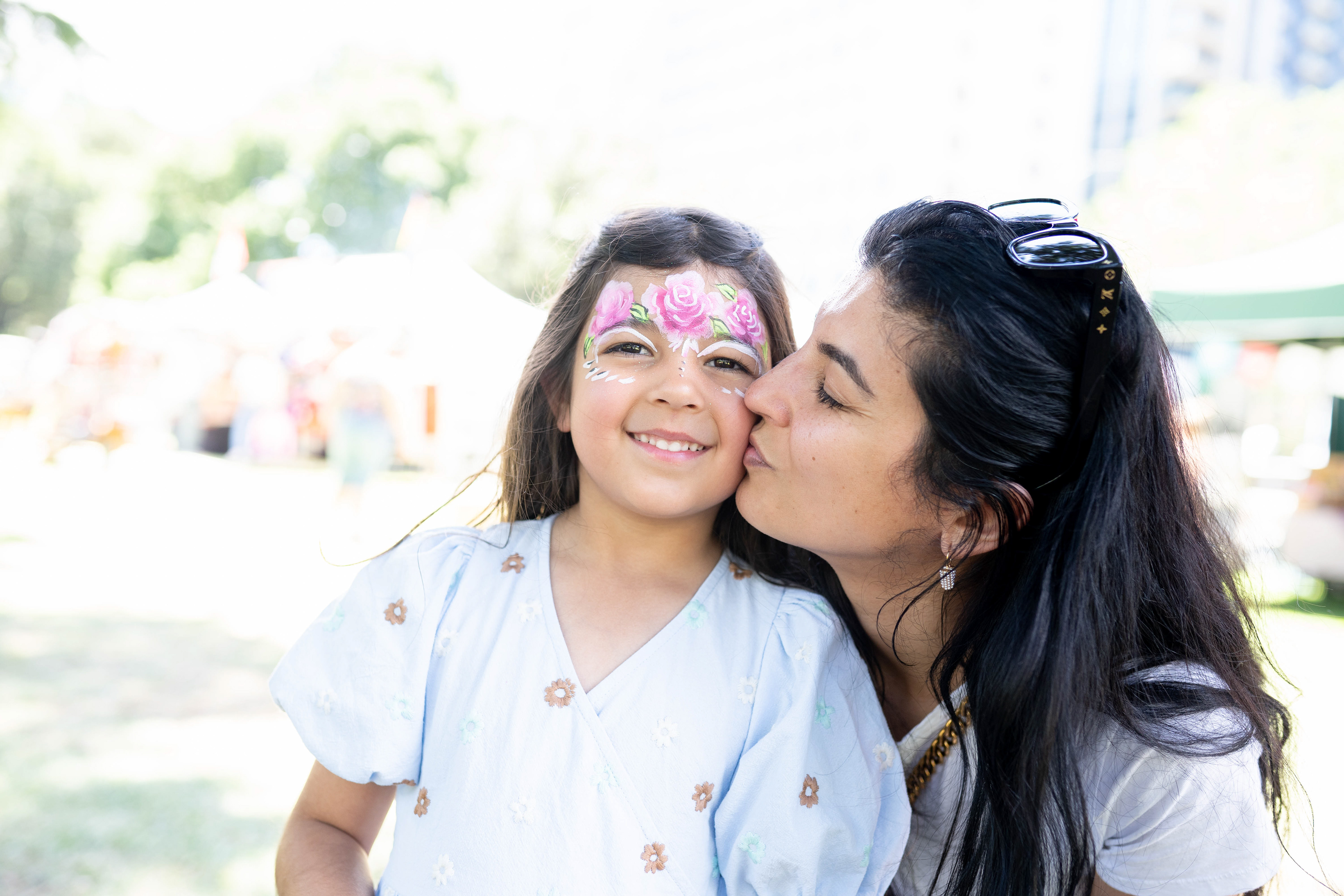 Parent kissing a child with colourful face paint