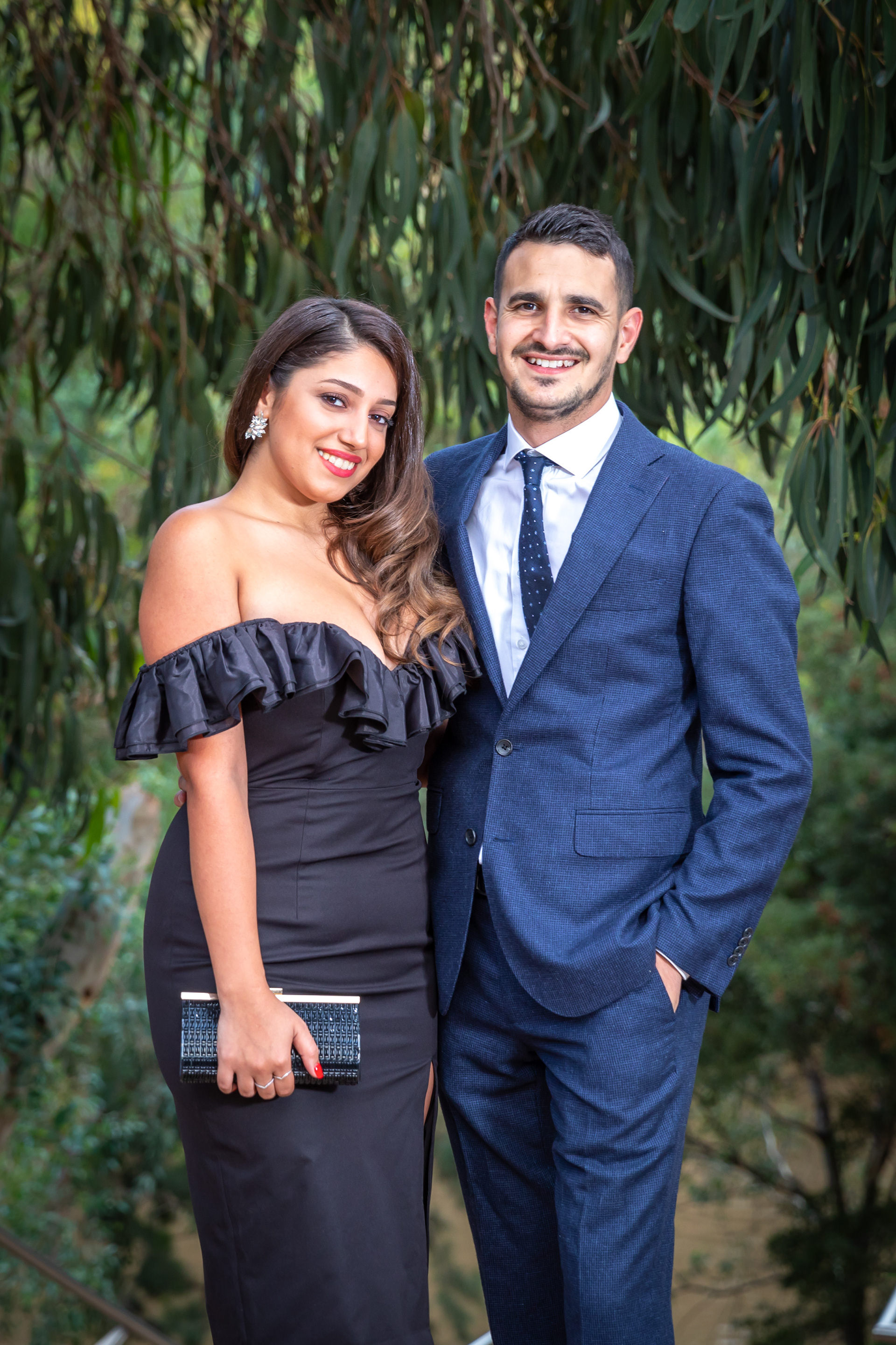 Couple in formal evening wear posing beside greenery