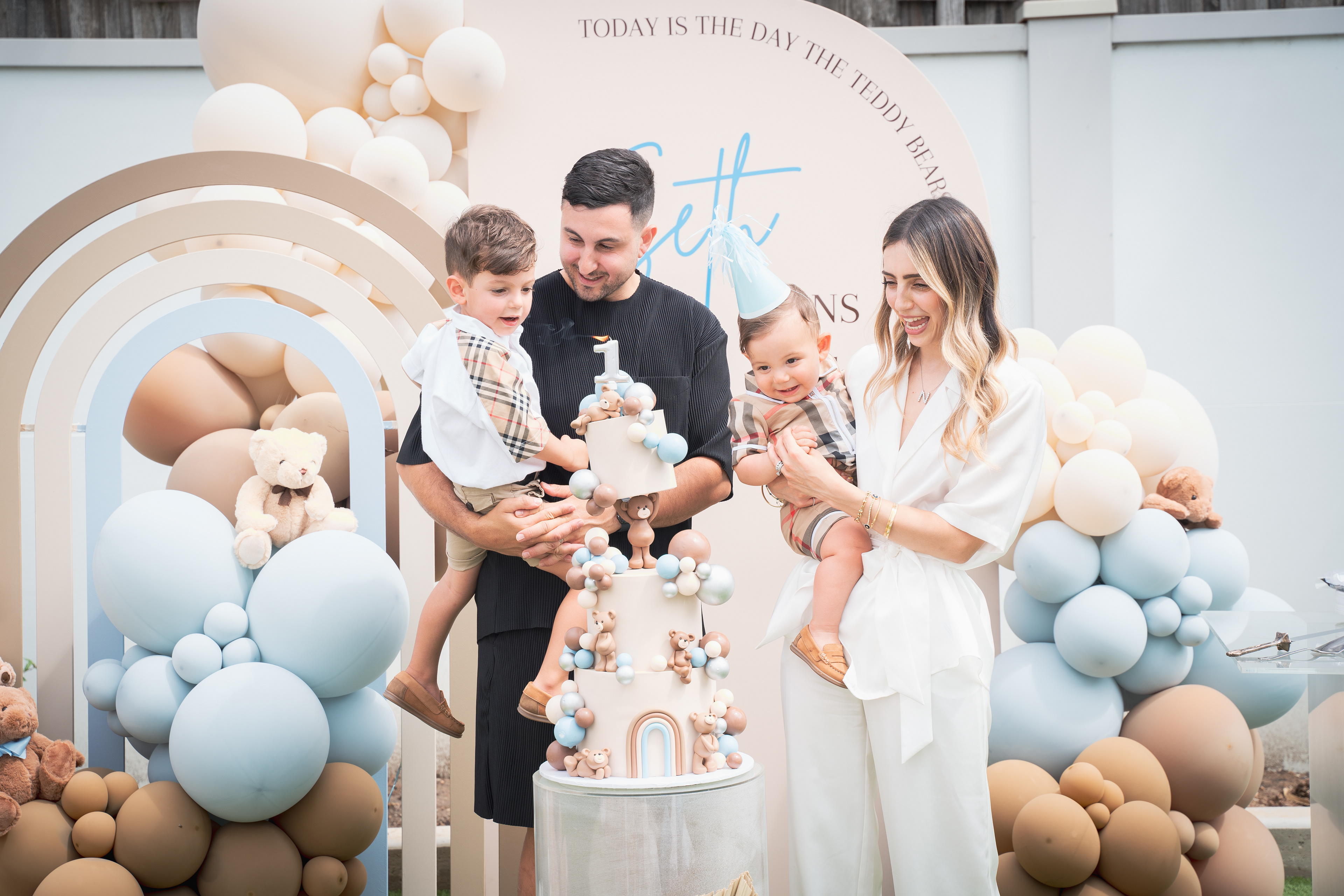 Family posing beside a cake and neutral-coloured balloon decorations