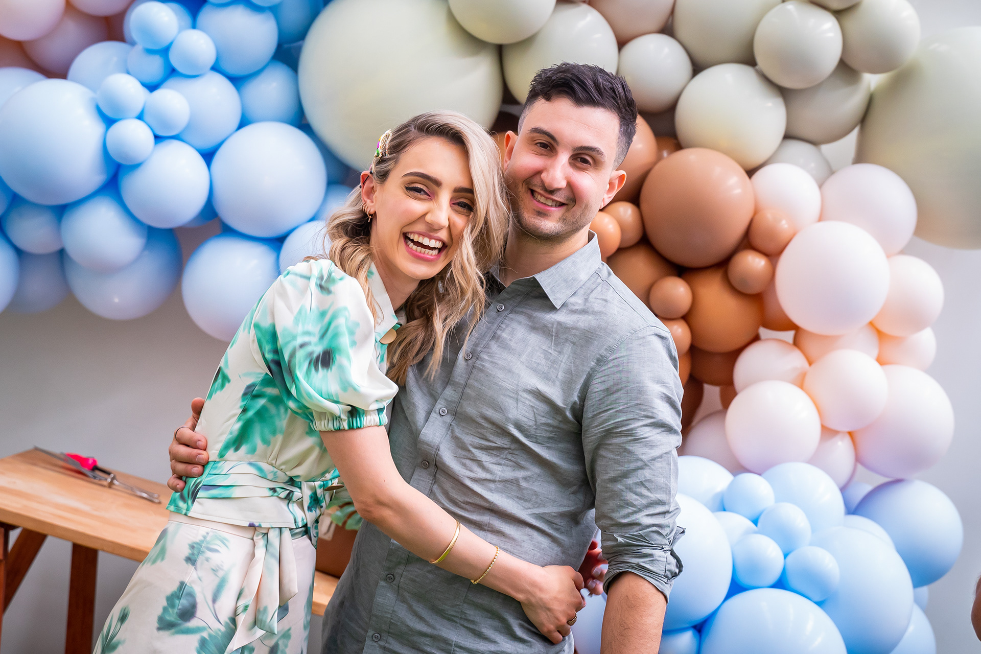 Couple smiling in front of a pastel balloon display